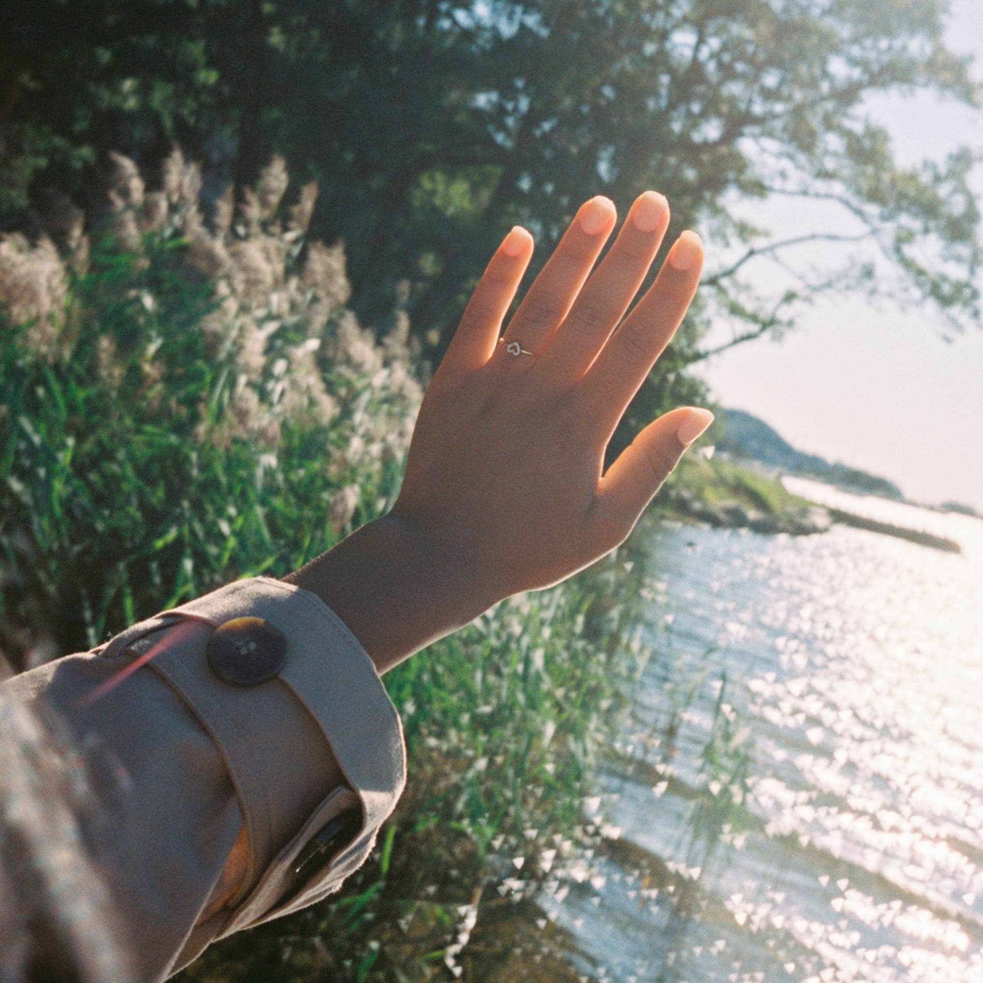 Sofie holder venstre hånd ut mot vannet og trærne. På ringfingeren har hun en hjerteformet ring med diamanter.