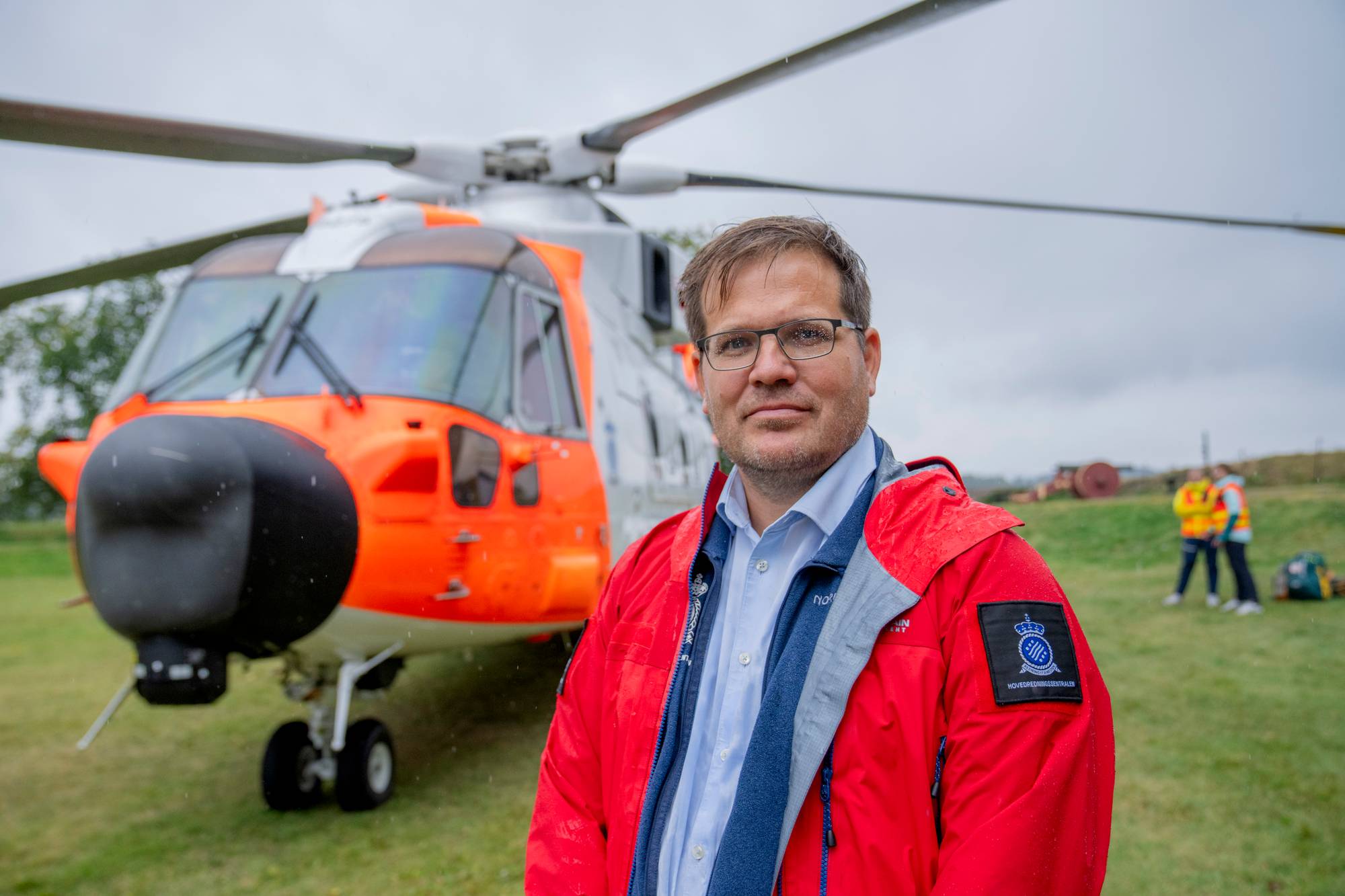 En mann i rød jakke står foran et redningshelikopter