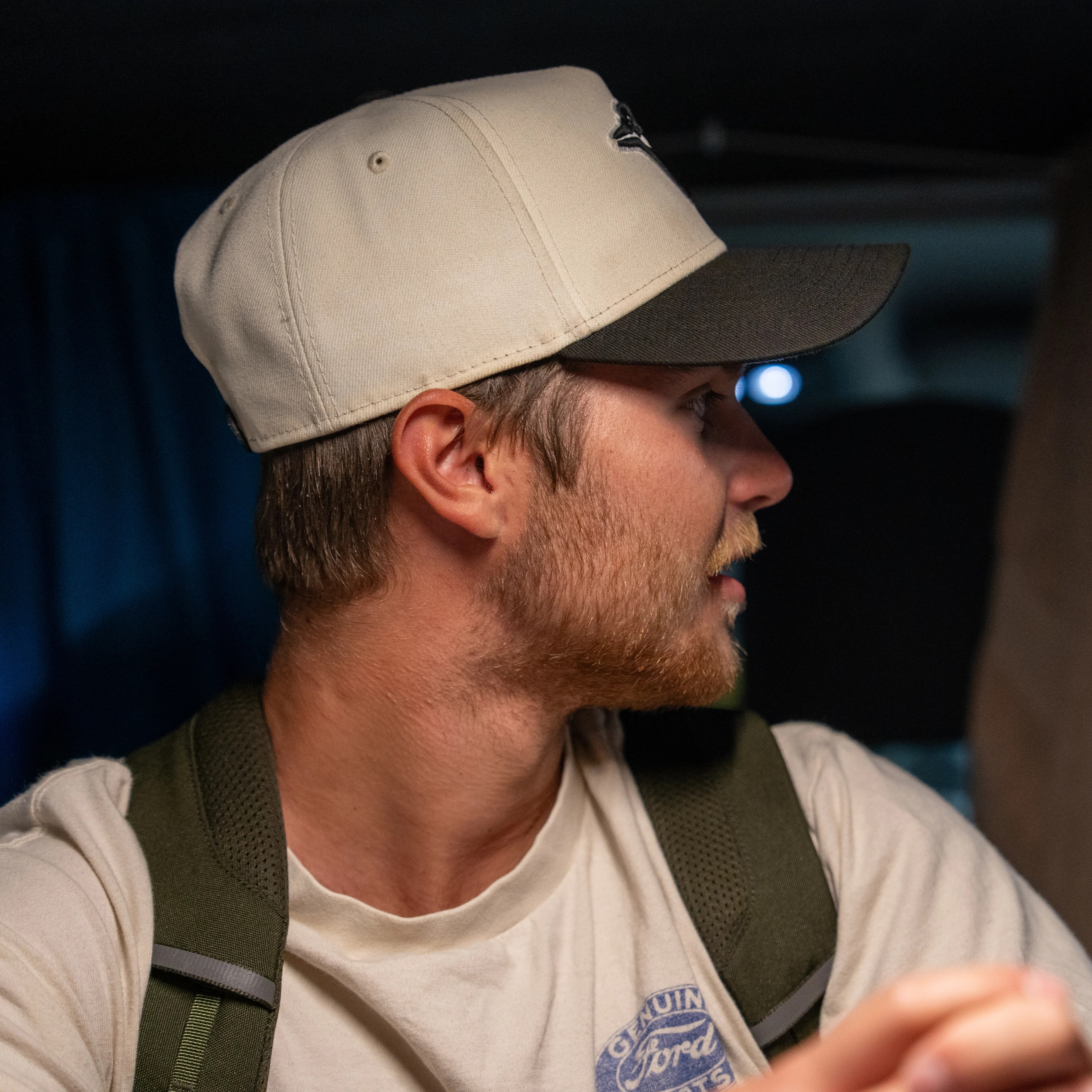 Mann med lys caps og grønn ryggsekk sett fra siden i et kjøretøy med blå gardiner.