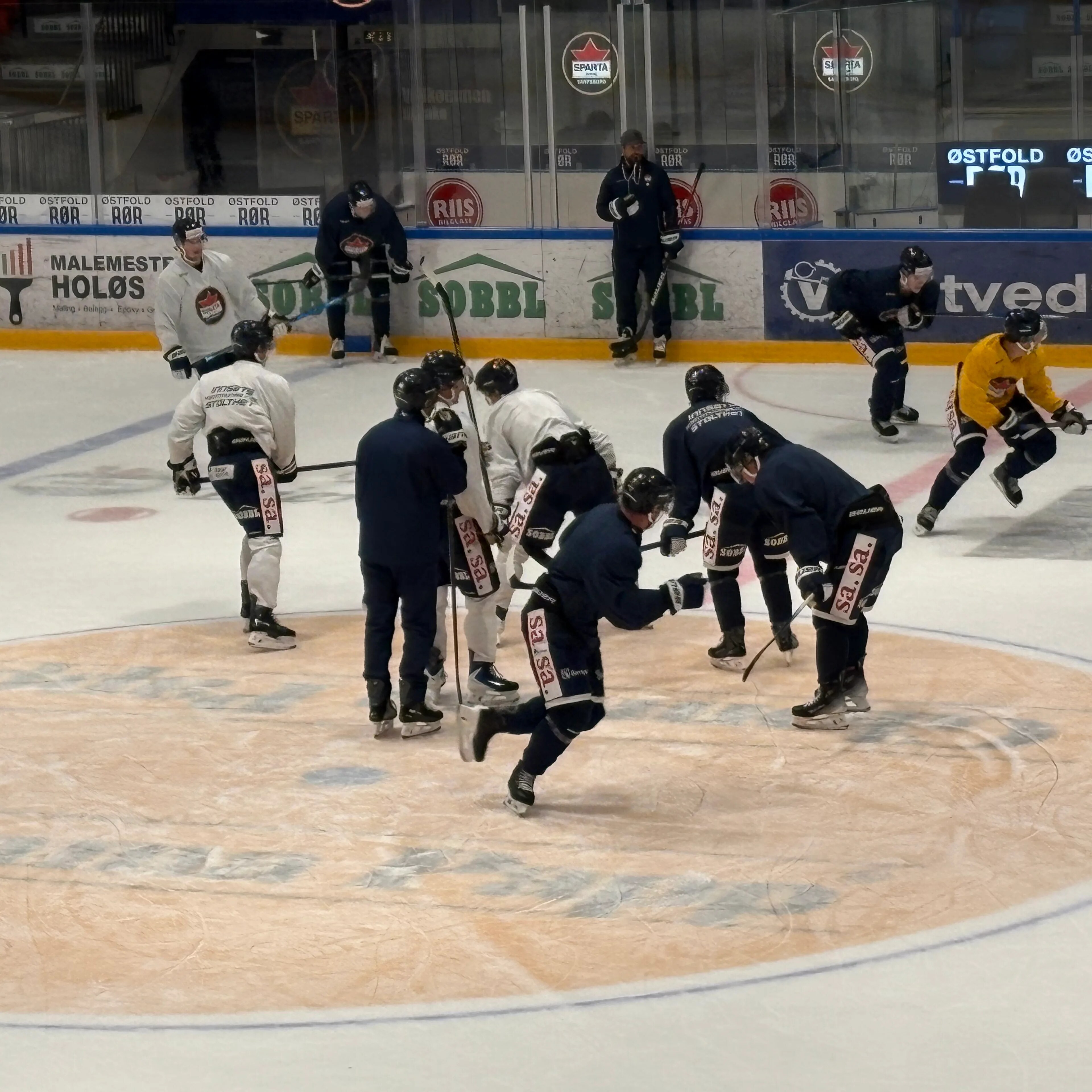Ishockeyspillere på trening på isflaten. Treneren står ved vantet og observerer. (Bildebeskrivelsen er laget av en KI-tjeneste)