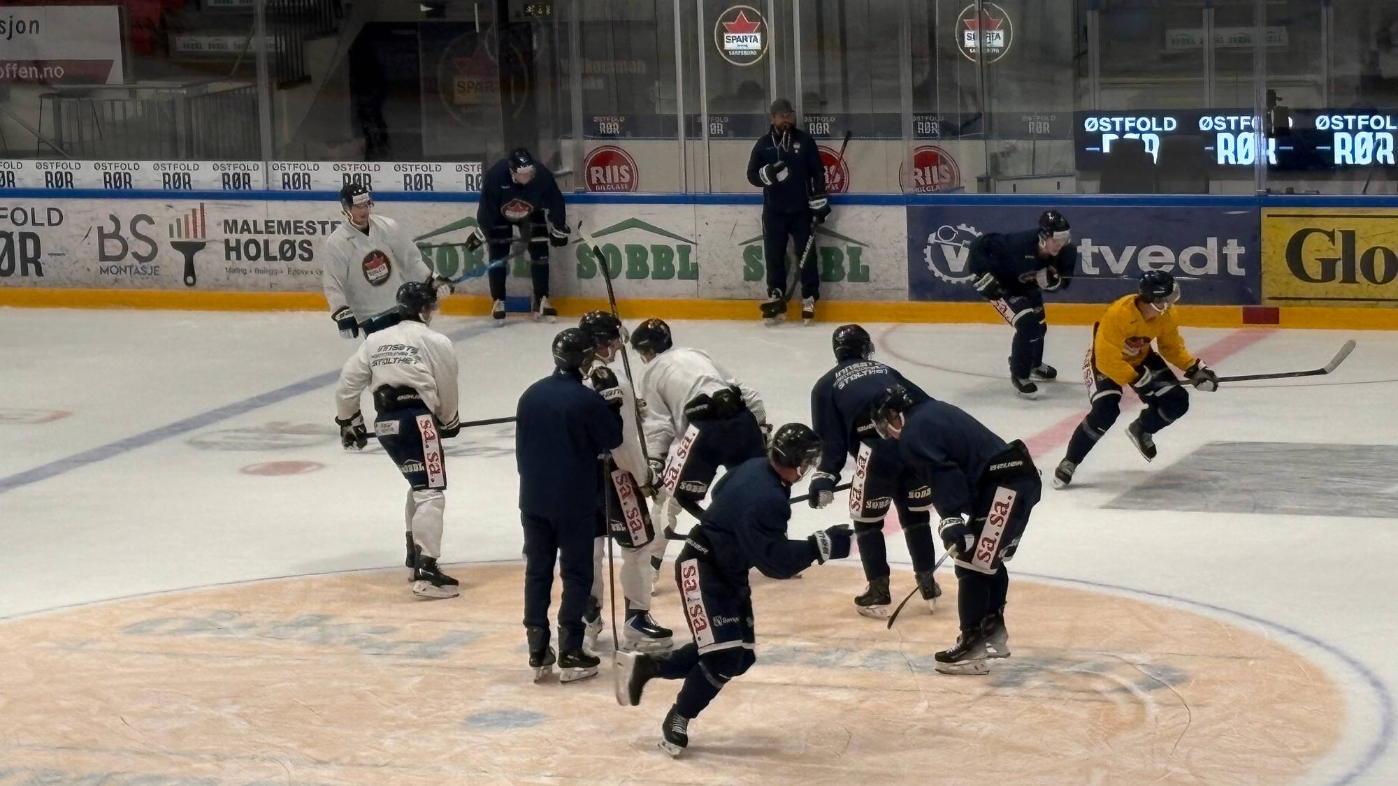 Ishockeyspillere på trening på isflaten. Treneren står ved vantet og observerer. (Bildebeskrivelsen er laget av en KI-tjeneste)