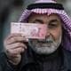 BAKR ALKASEM / AFP / NTB En mann holder opp en ti-dinars seddel foran seg. Han har på seg en mørk jakke og en tradisjonell hodebekledning. Bakgrunnen er uklar, men antyder en urban setting. Bildet kan brukes i sammenheng med økonomiske spørsmål eller handel. (Bildebeskrivelsen er laget av en KI-tjeneste)