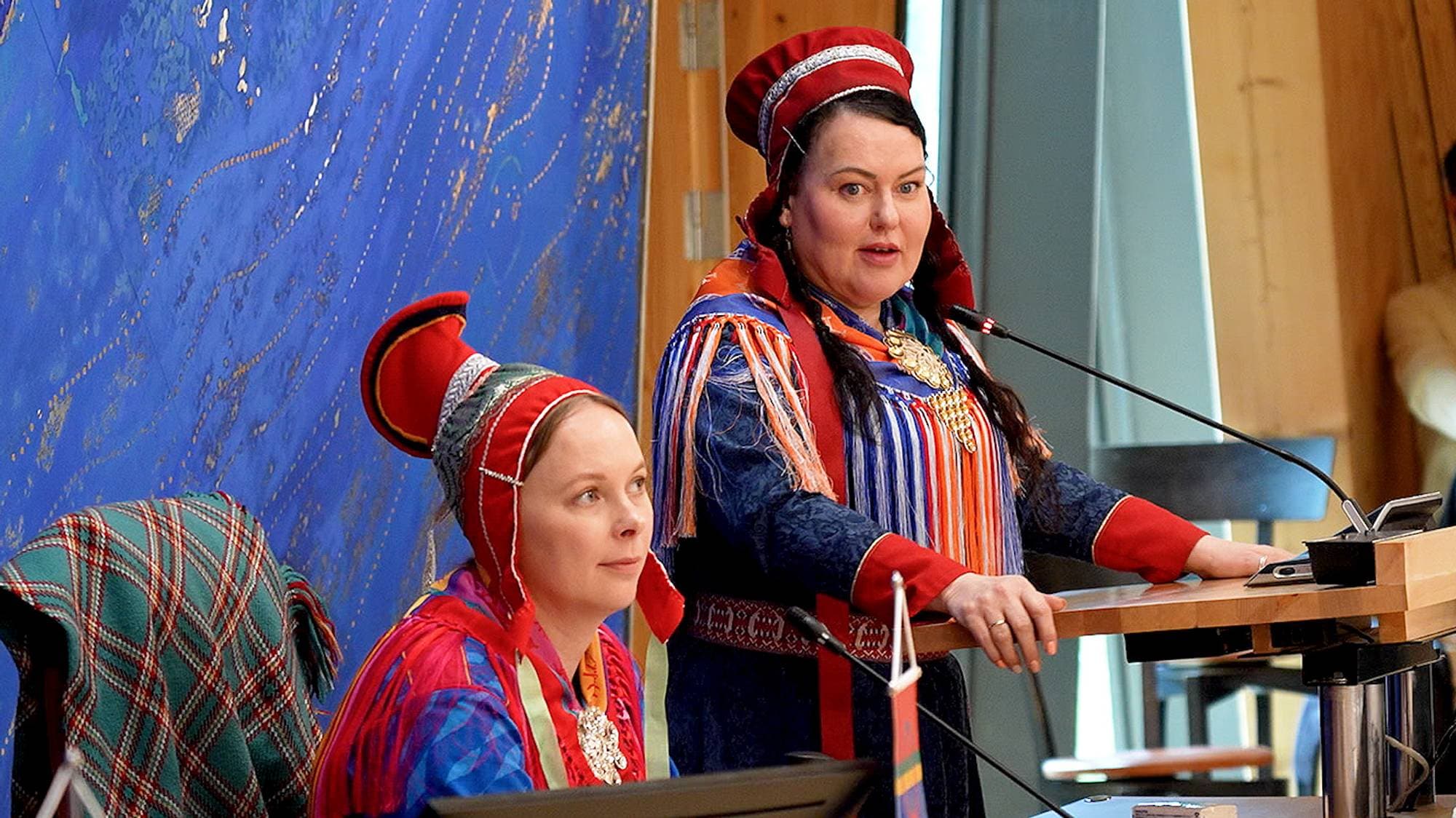 Kvinnelig møteleder med en kvinne ved siden av seg på talerstolen
