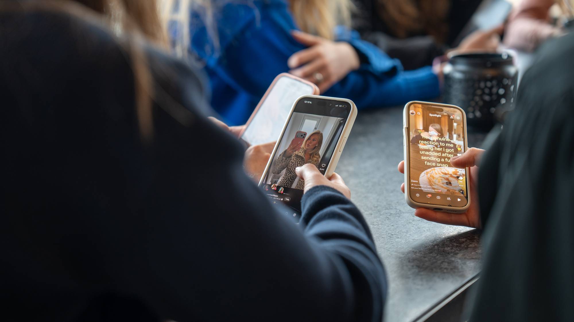 Personer sitter rundt et bord og bruker mobiltelefoner med sosiale medier. (Bildebeskrivelsen er laget av en KI-tjeneste)