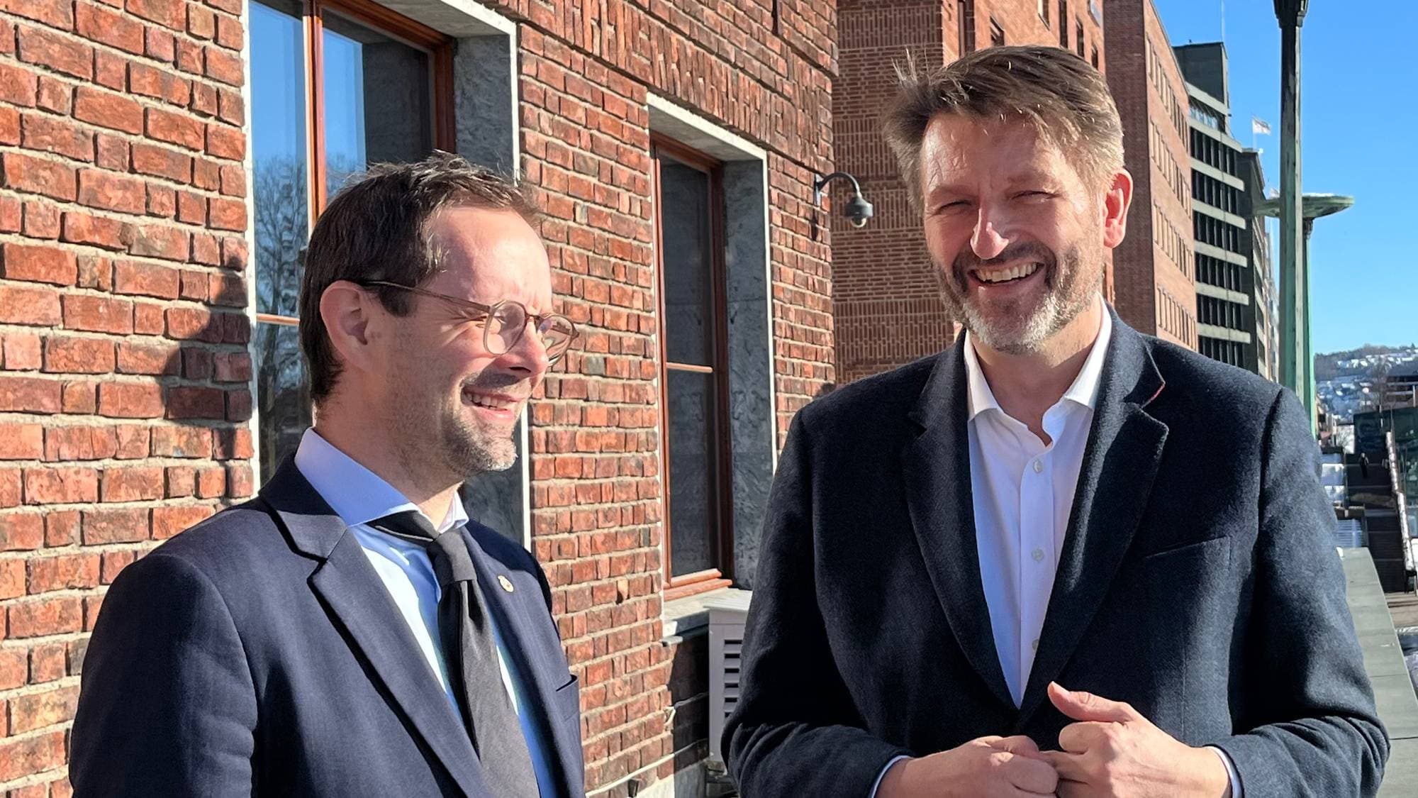 Finansbyråd Hallstein Bjercke og byrådsleder Eirik Lae Solberg smiler på balkongen utenfor rådhuset.