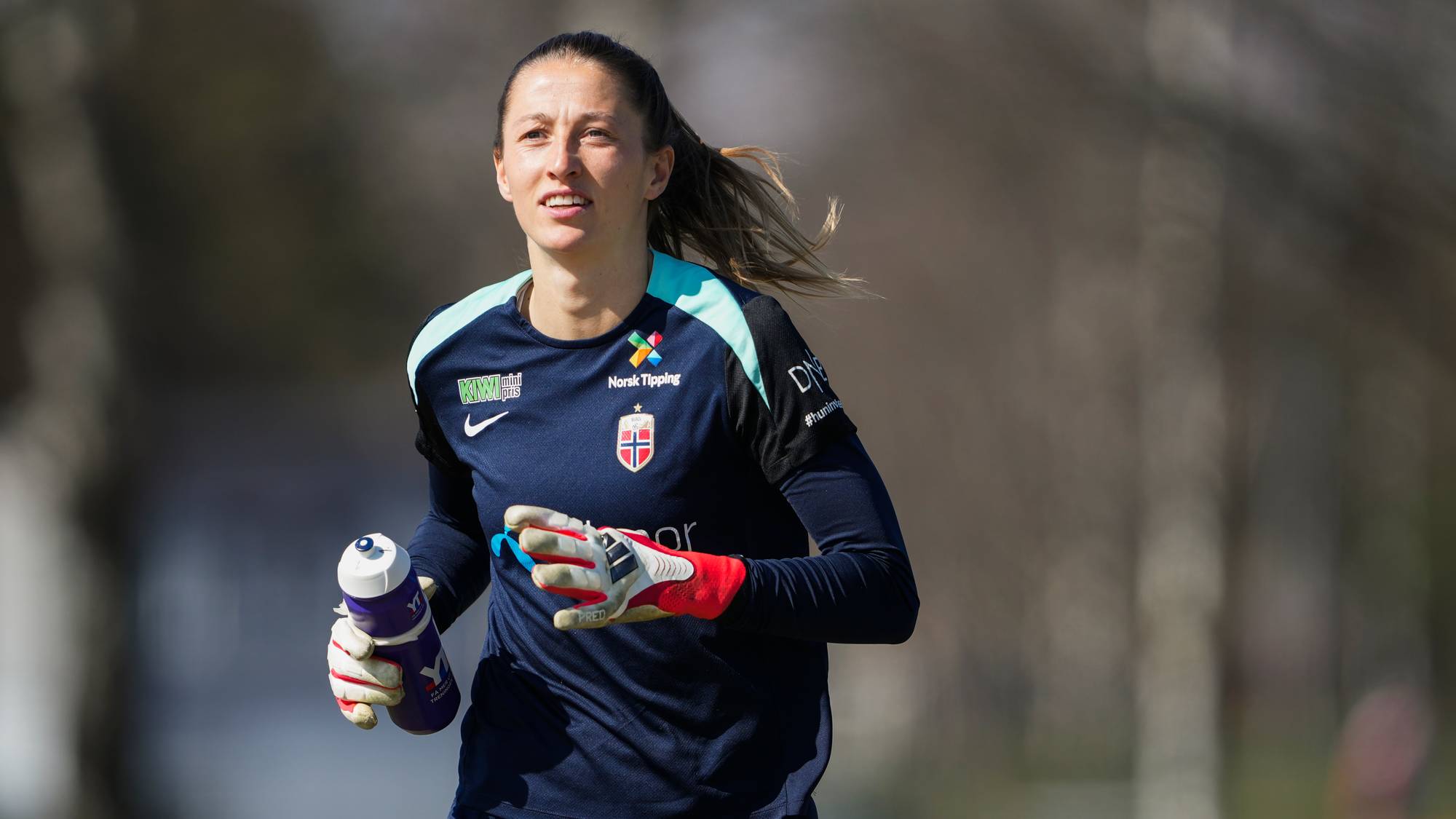 Fotballkeeper Aurora Mikalsen jogger på treningsfeltet med en drikkeflaske. (Bildebeskrivelsen er laget av en KI-tjeneste)