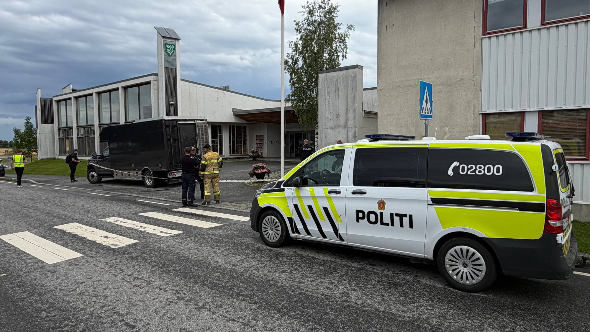 Politibil og brannmann står utenfor en bygning sammen med en svart tilhenger og politi. 