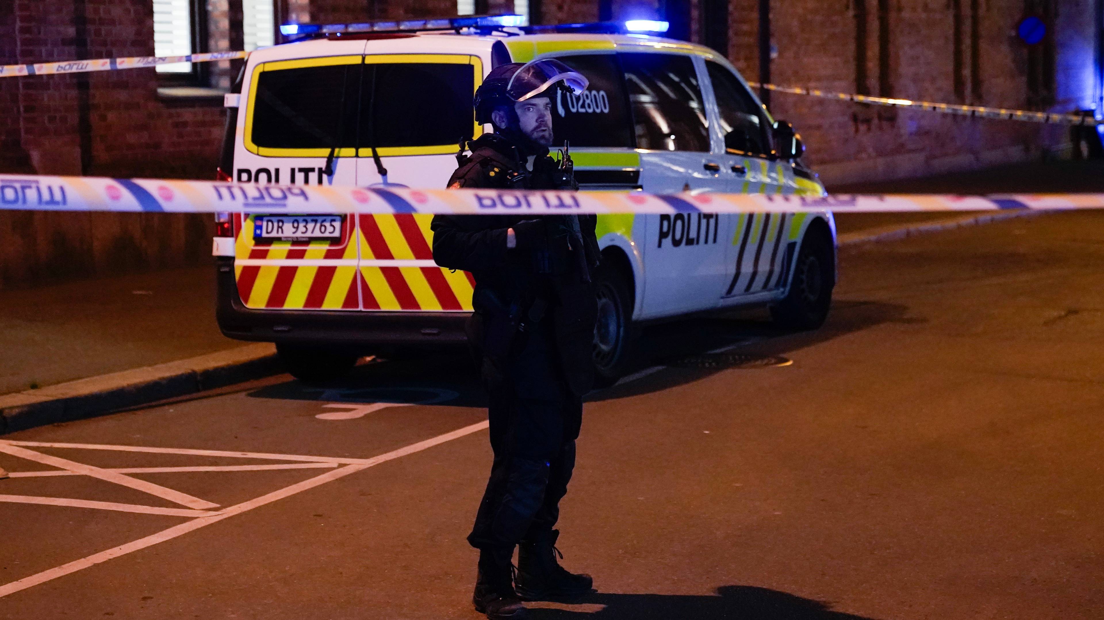 en politimann som står foran en politibil, innenfor en sperring