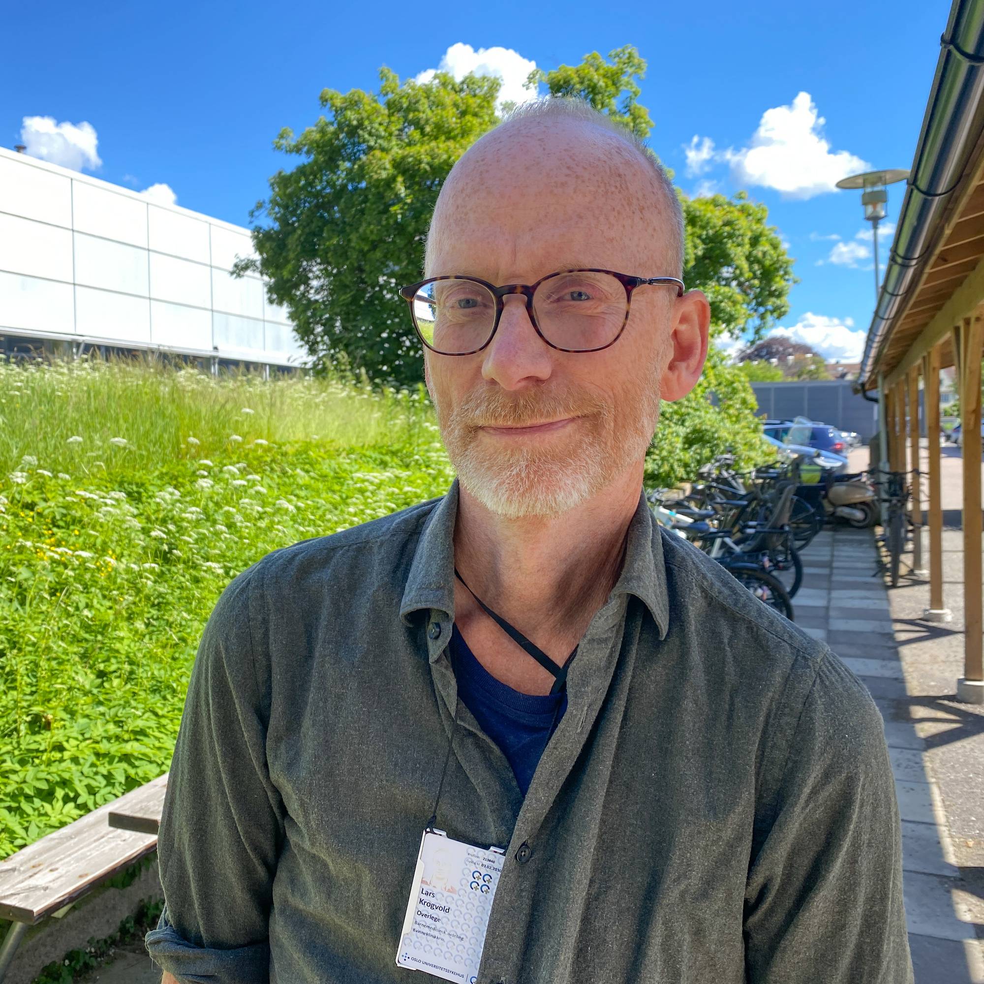 En hårløs mann med briller og lyst skjegg ser i kamera. Han har på seg en grønn skjrote og rundt halsen henger et nøkkelkort.
