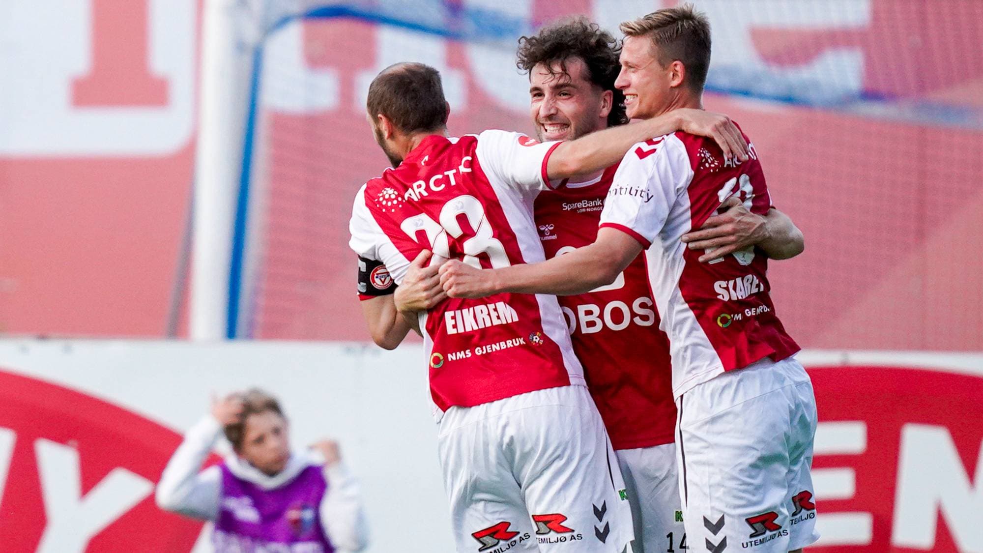 Fotballspillere fra Tromsø IL feirer en scoring med en klem på fotballbanen. (Bildebeskrivelsen er laget av en KI-tjeneste)
