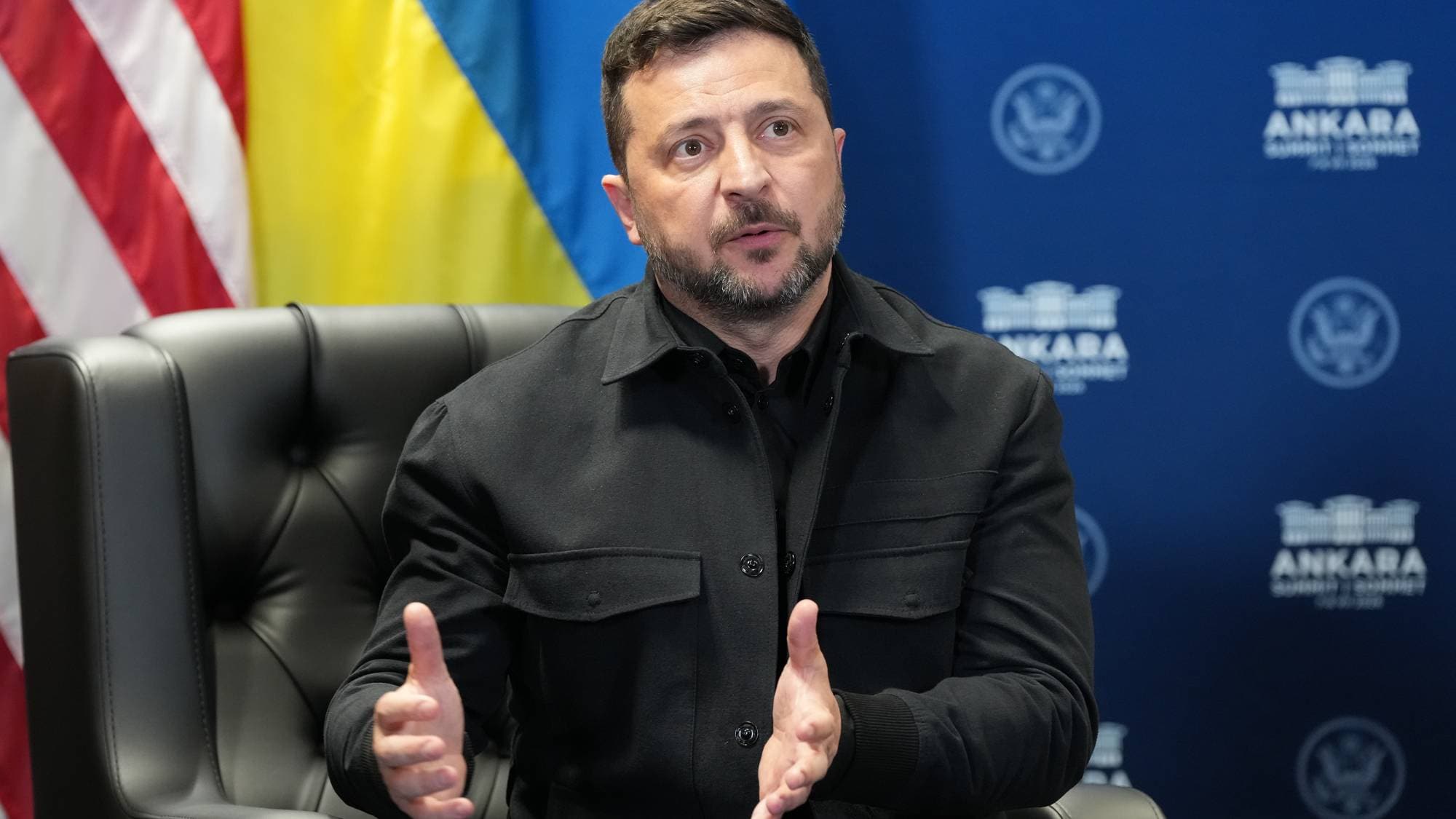 Volodymyr Zelenskyj sitter i en stol foran flaggene til USA og Ukraina. (Bildebeskrivelsen er laget av en KI-tjeneste)