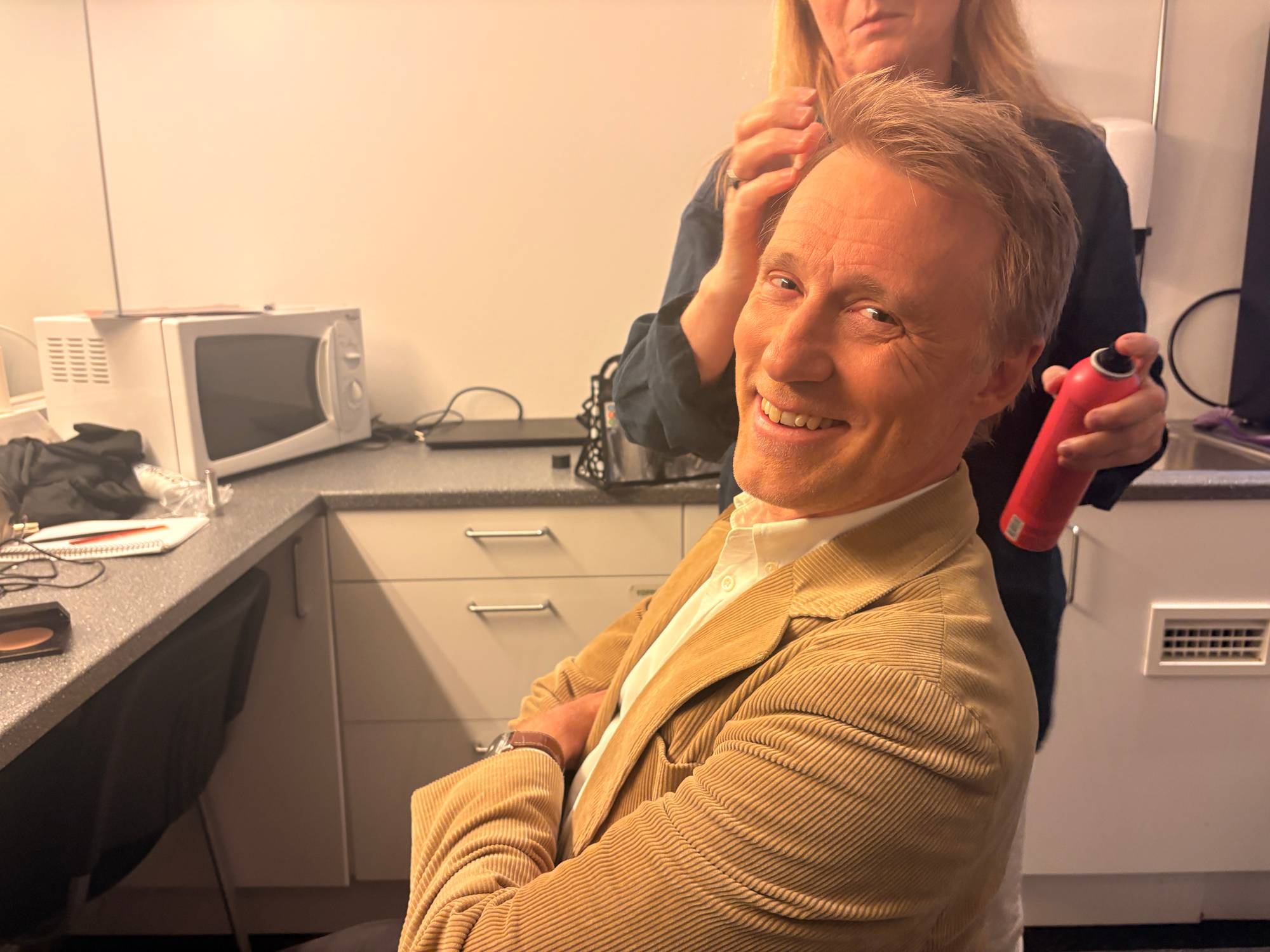 En mann i blazer og skjorte blir sminket. 