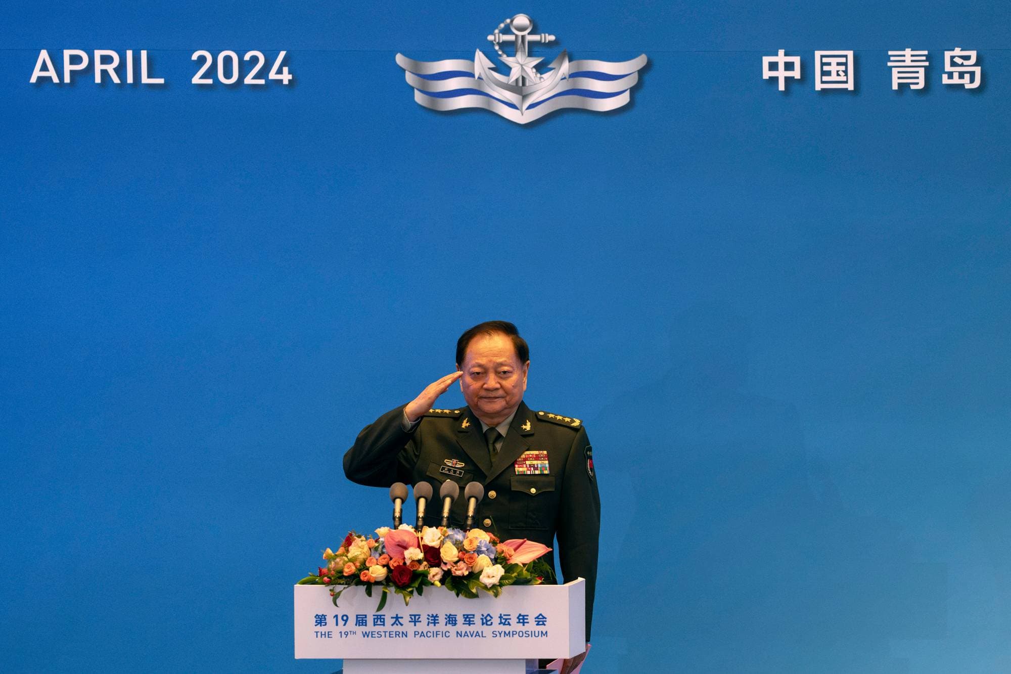 Kinesisk offiser i uniform gjør honnør ved talerstol under Western Pacific Naval Symposium i Qingdao. (Bildebeskrivelsen er laget av en KI-tjeneste)
