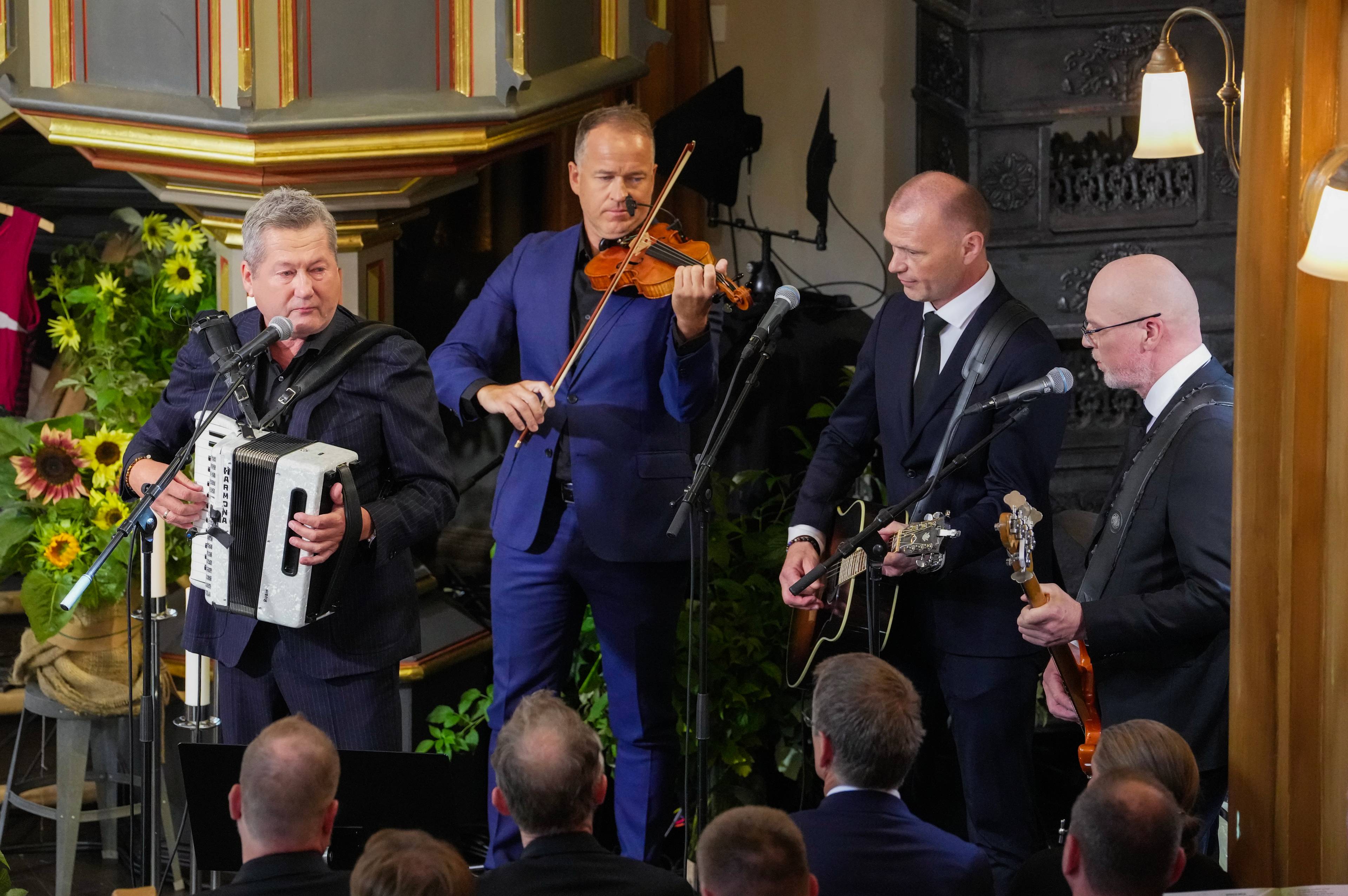Fire musikere spiller instrumenter for et publikum i en kirke.