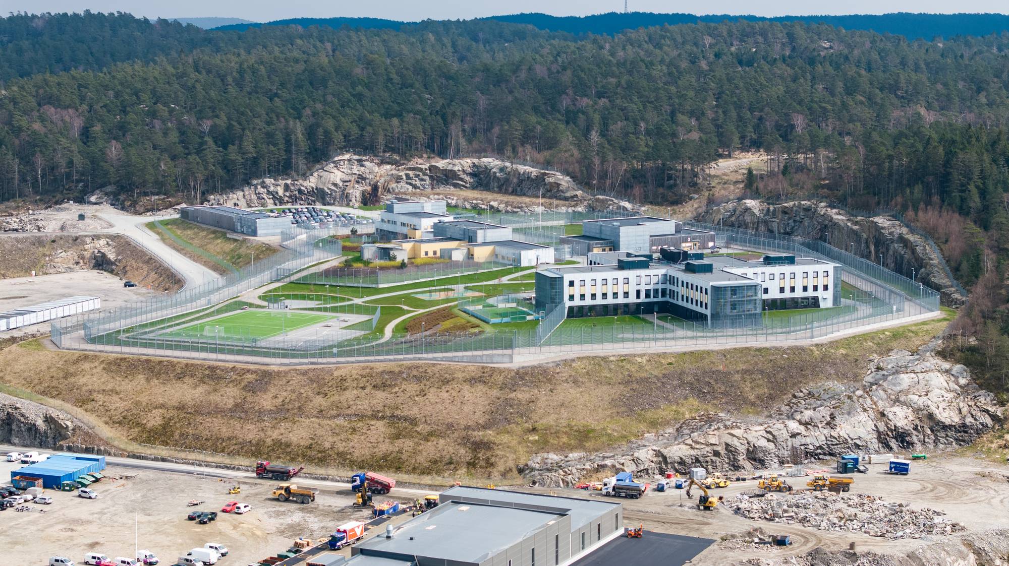 Luftfoto av Agder fengsel, avdeling Mandal, med bygninger, uteområder og gjerder i et skogsområde. (Bildebeskrivelsen er laget av en KI-tjeneste)