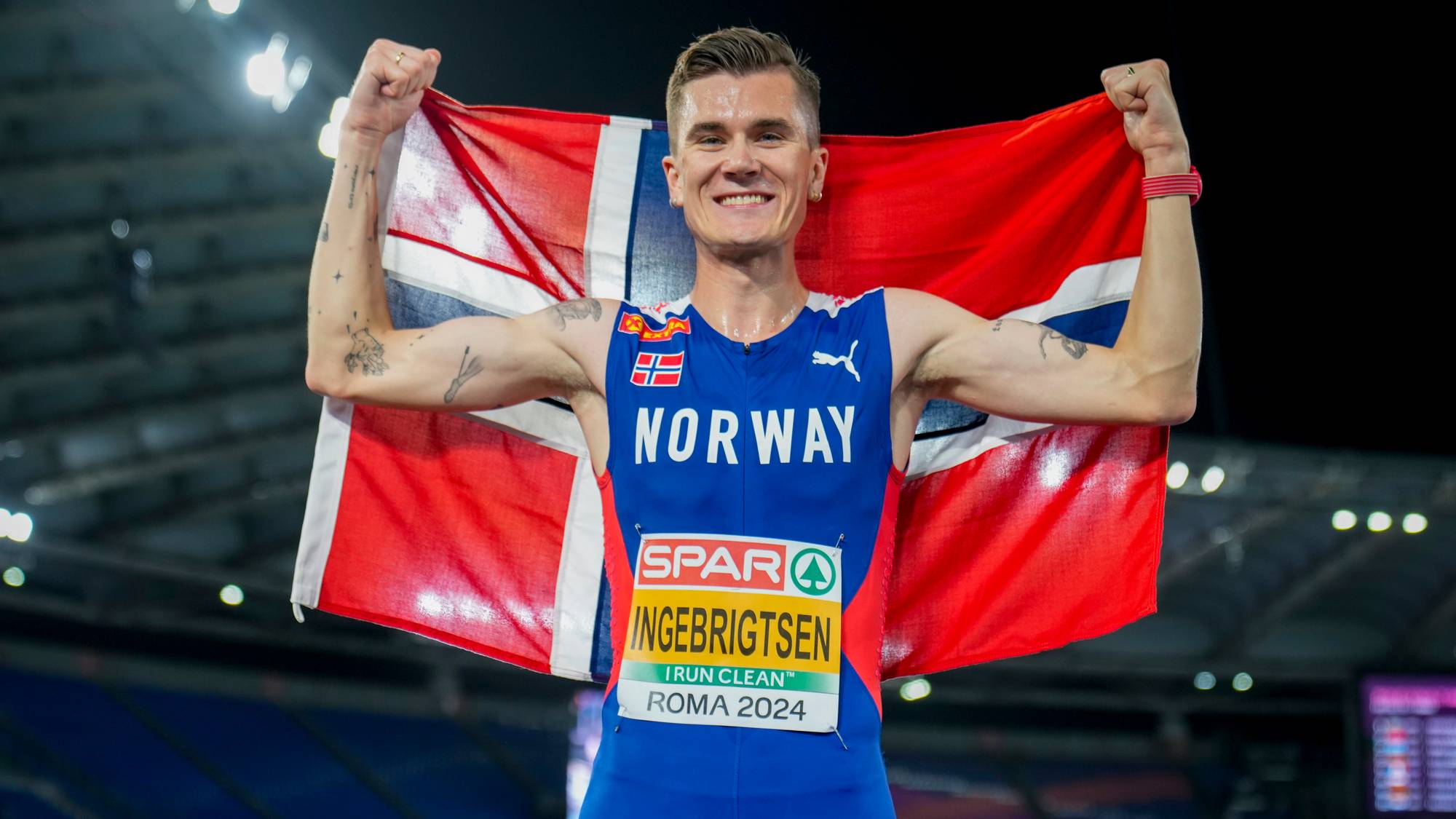 Jakob Ingebrigtsen feirer med norsk flagg på stadion etter EM i Roma 2024. (Bildebeskrivelsen er laget av en KI-tjeneste)