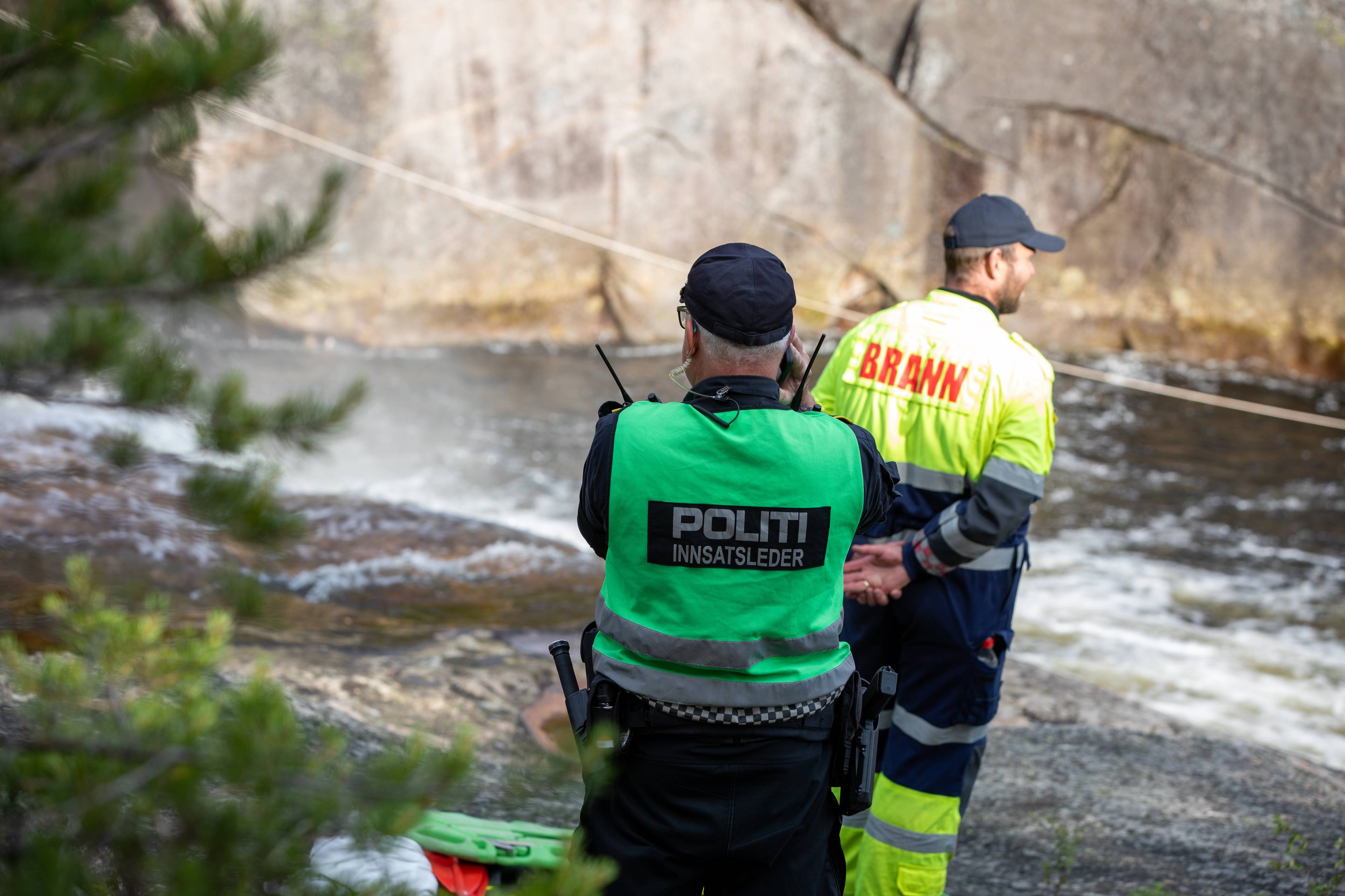 Politiets innsatsleder og en brannkonstabel står ved en elv under en redningsaksjon. (Bildebeskrivelsen er laget av en KI-tjeneste)