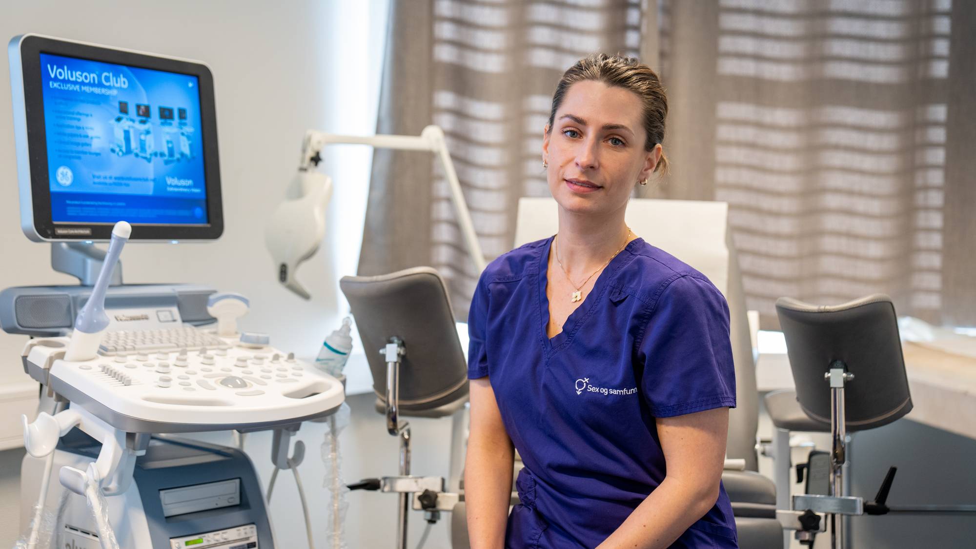 Lege Siri Kløkstad sitter i et undersøkelsesrom ved Sex og samfunn sin klinikk i Oslo. Hun har på seg blå legeklær. I bakgrunnen er det en ultralydmaskin og undersøkelsesbenk.