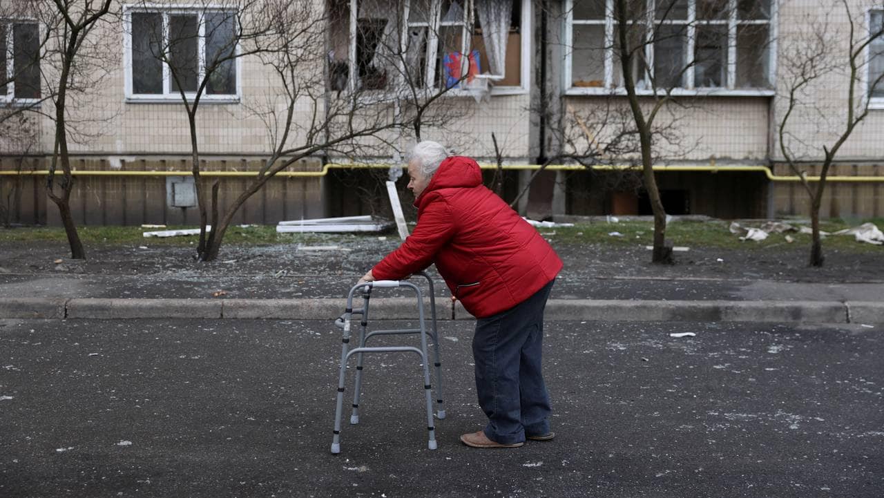 En eldre kvinne går forbi en boligblokk som ble skadd i et rakettangrep i Kyiv.