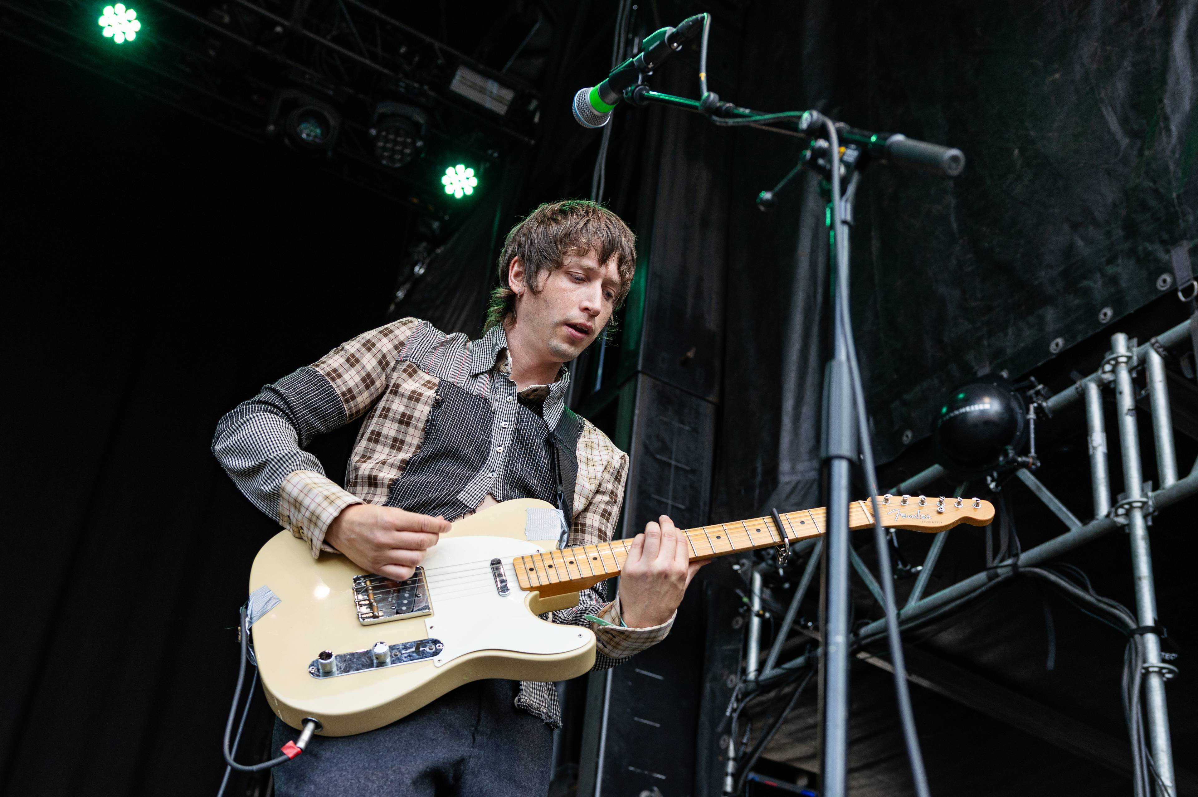 Mann spiller elektrisk gitar på en scene foran svart bakteppe.