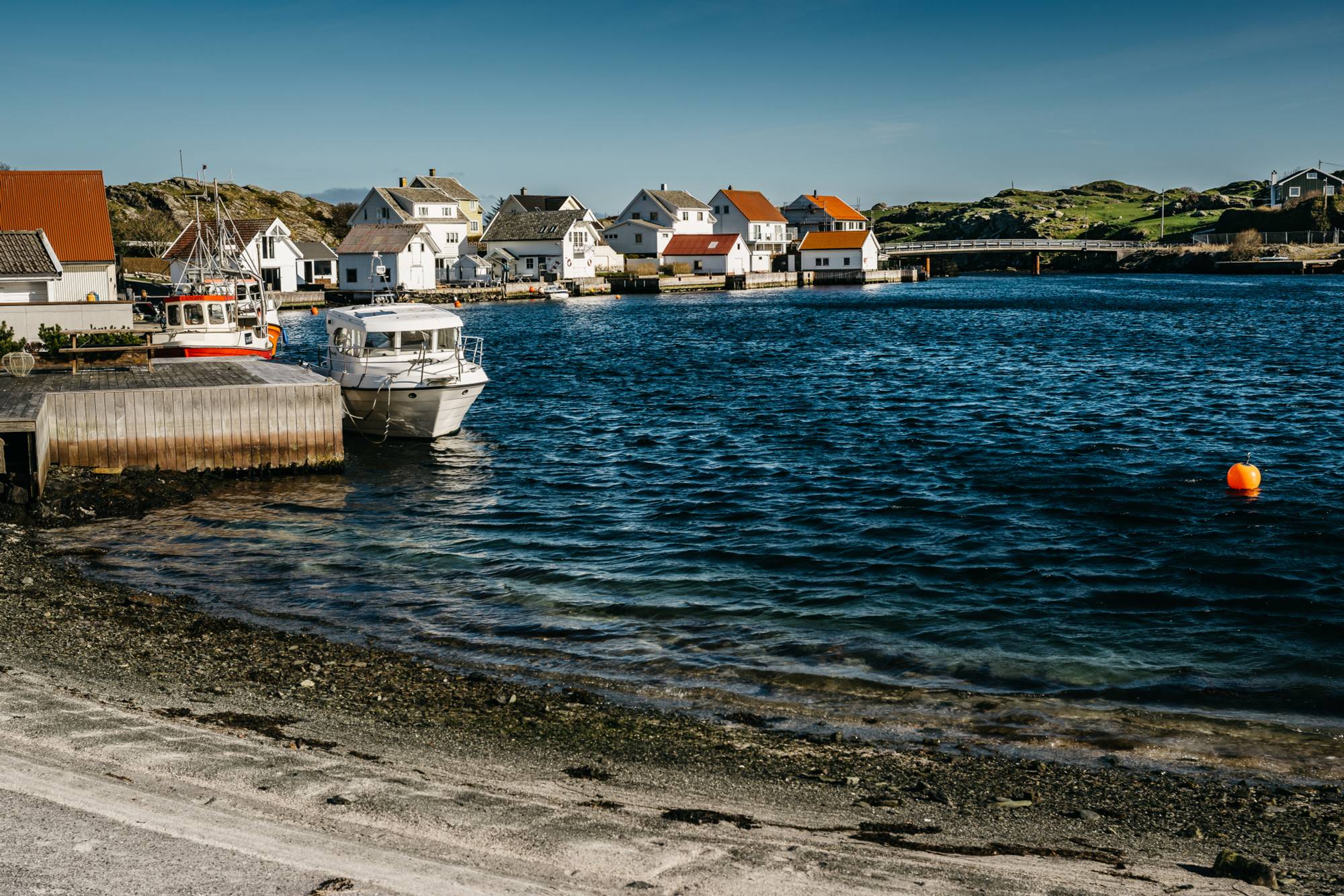En liten strand, fiskebåter som ligger fortøyd langs brygger og hvite trehus.
