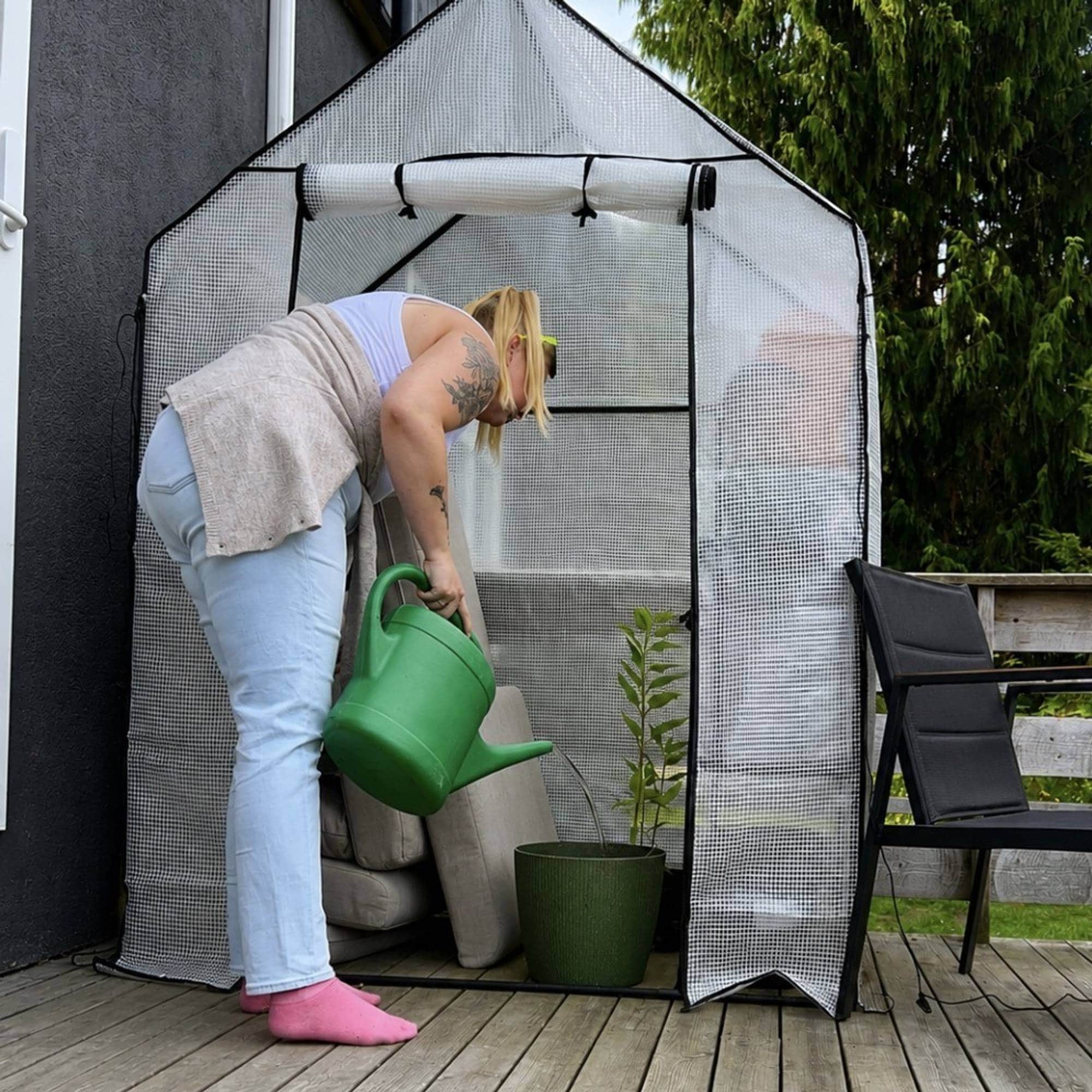 Kvinne står ved drivhus og vanner plantene