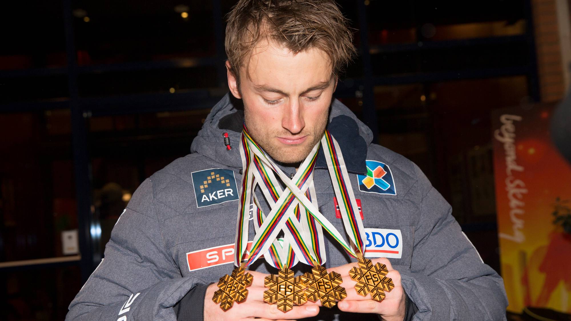 Petter Northug ser ned på fire gullmedaljer som han holder i hendene. (Bildebeskrivelsen er laget av en KI-tjeneste)
