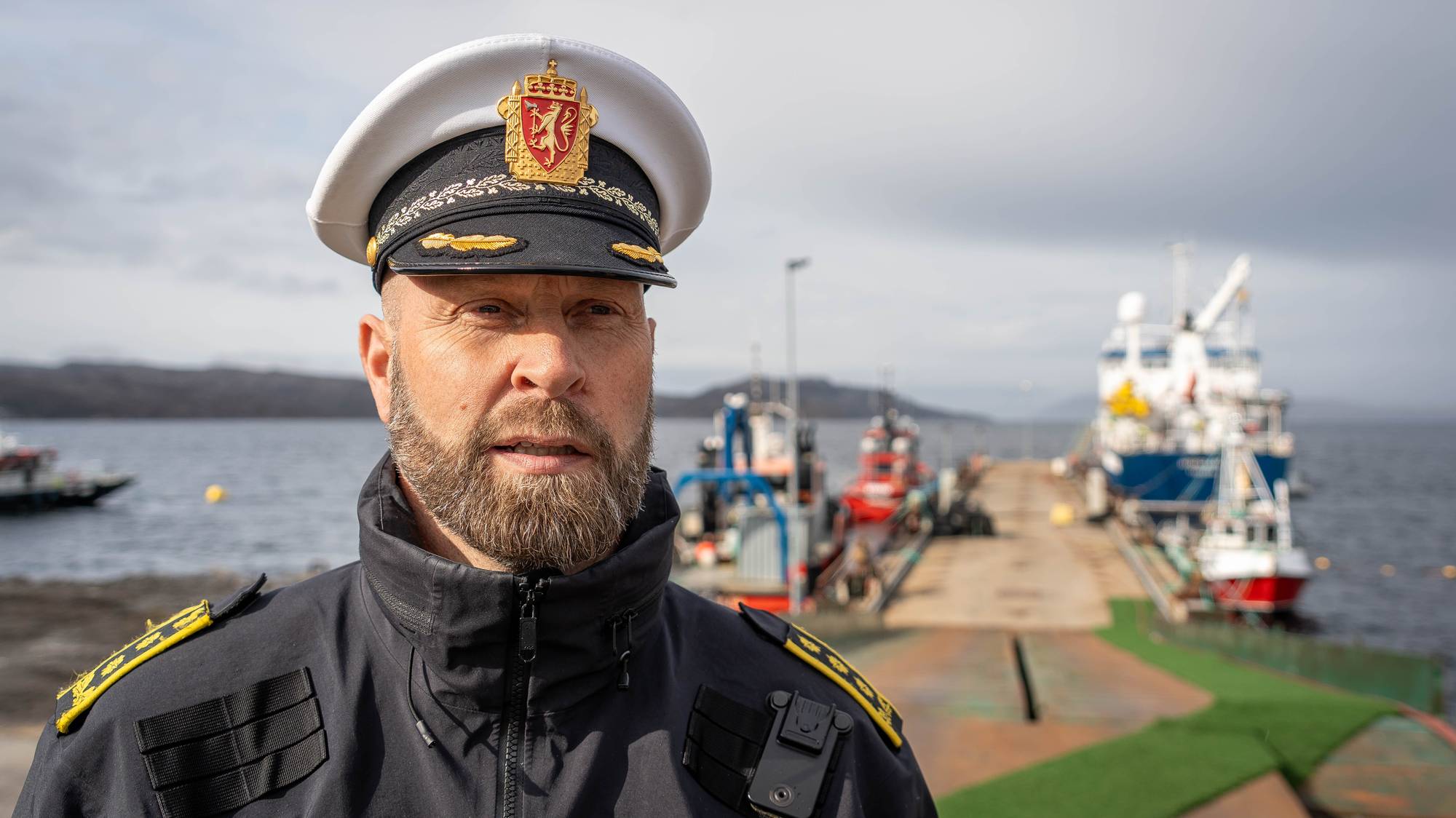 Mann i politiuniform foran flytebrygge hvor det ligger flere fartøy.