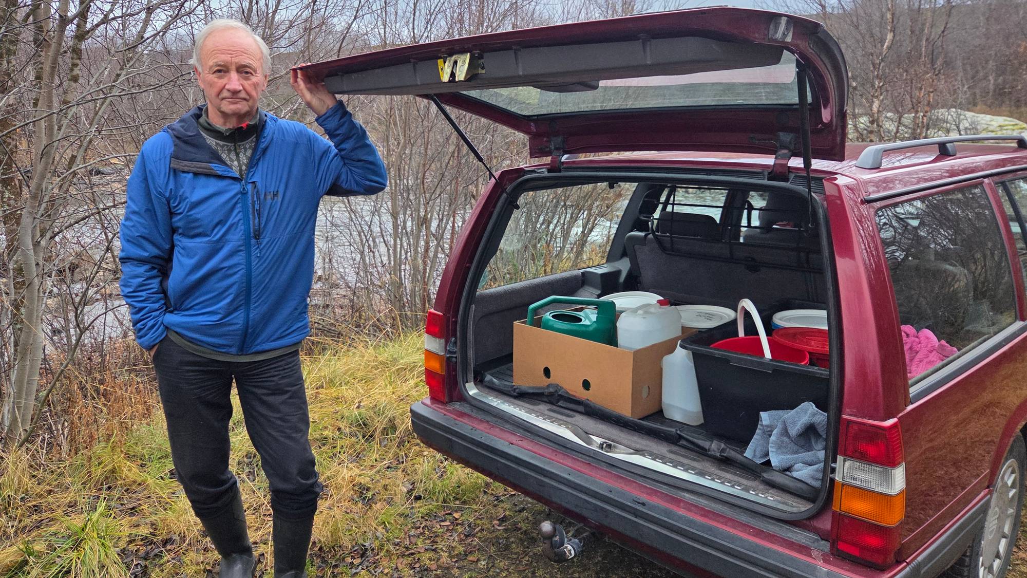 Kjell Næss står ved bilen og viser bagasjerommet med vann og utstyr. Han har samlet vann fra Sandneselva på grunn av vannmangel. 
