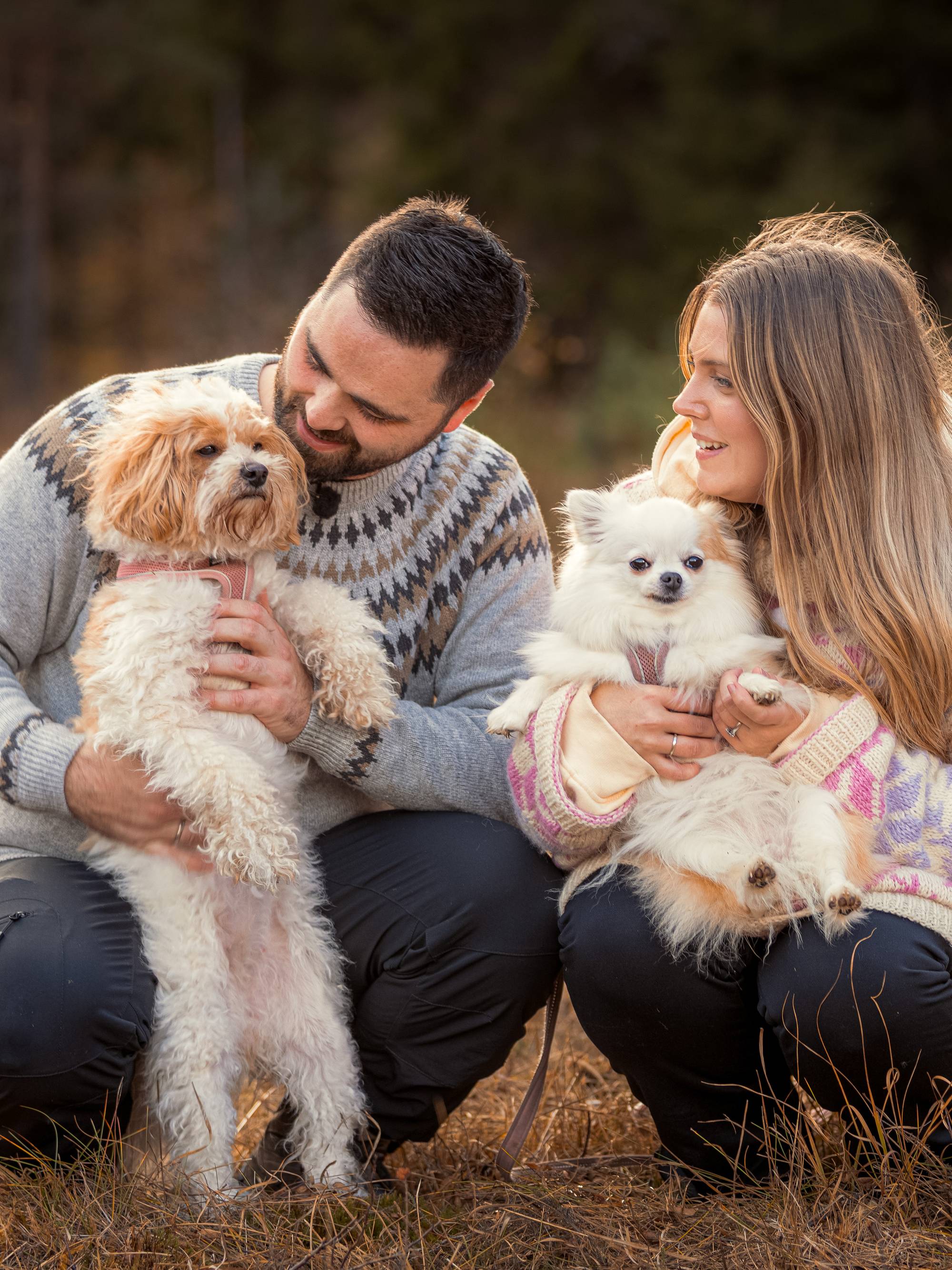 Aleksander og Jeanette sitter på huk ute. De holder hver sin hund. Aleksander holder Lilli. Hun har brun og hvit pels, og står på bakbeina. Aleksander ser ned på Lilli. Jeanette holder Stella, som også har brun og hvit pels, på fanget. Jeanette ser bort på Lilli. 