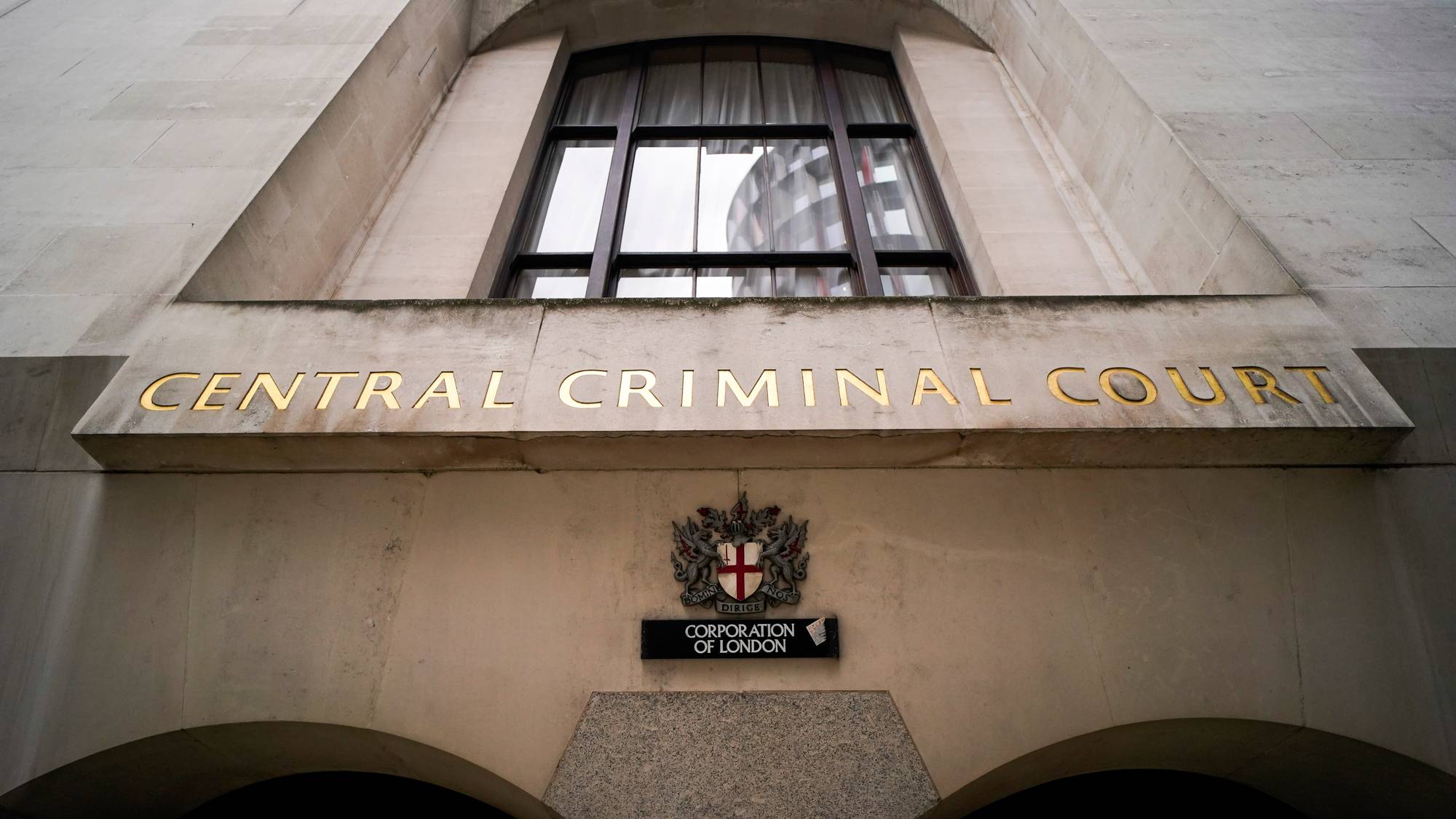 Bildet viser fasaden av Central Criminal Court i London. Overskriften "CENTRAL CRIMINAL COURT" er skrevet med gullbokstaver over inngangen. Under det er det et skilt med teksten "CORPORATION OF LONDON", samt et symbol med et skjold. Bygningens arkitektur er preget av grå steinflater. (Bildebeskrivelsen er laget av en KI-tjeneste)