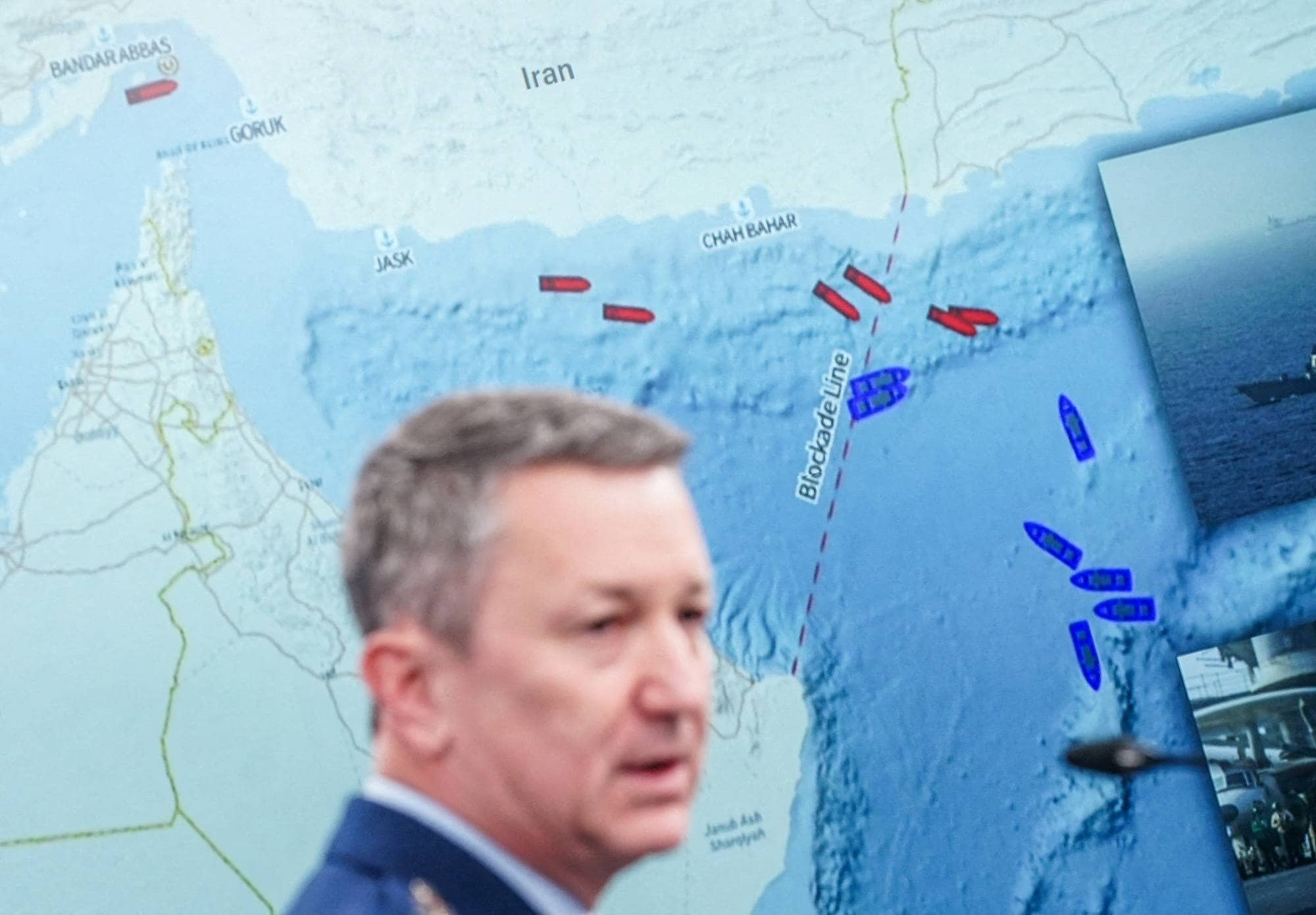 Et kart viser en blokkadelinje i Hormuzstredet. En mann i militæruniform står foran et kart. Det er også et bilde av et krigsskip. (Bildebeskrivelsen er laget av en KI-tjeneste)