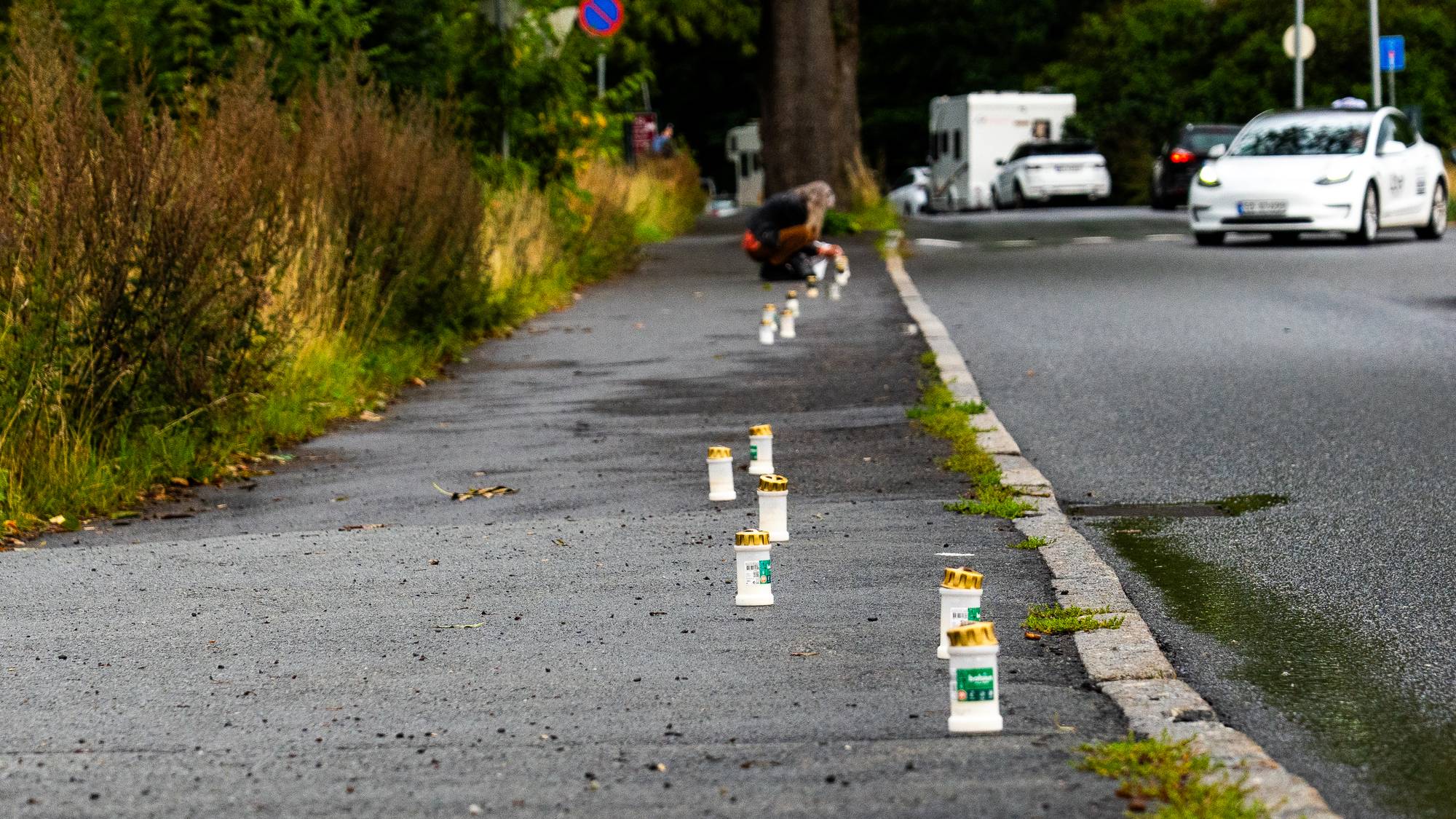 Gravlys plassert på rad langs en gangvei ved en vei med biler. En person sitter bøyd lenger fremme. (Bildebeskrivelsen er laget av en KI-tjeneste)