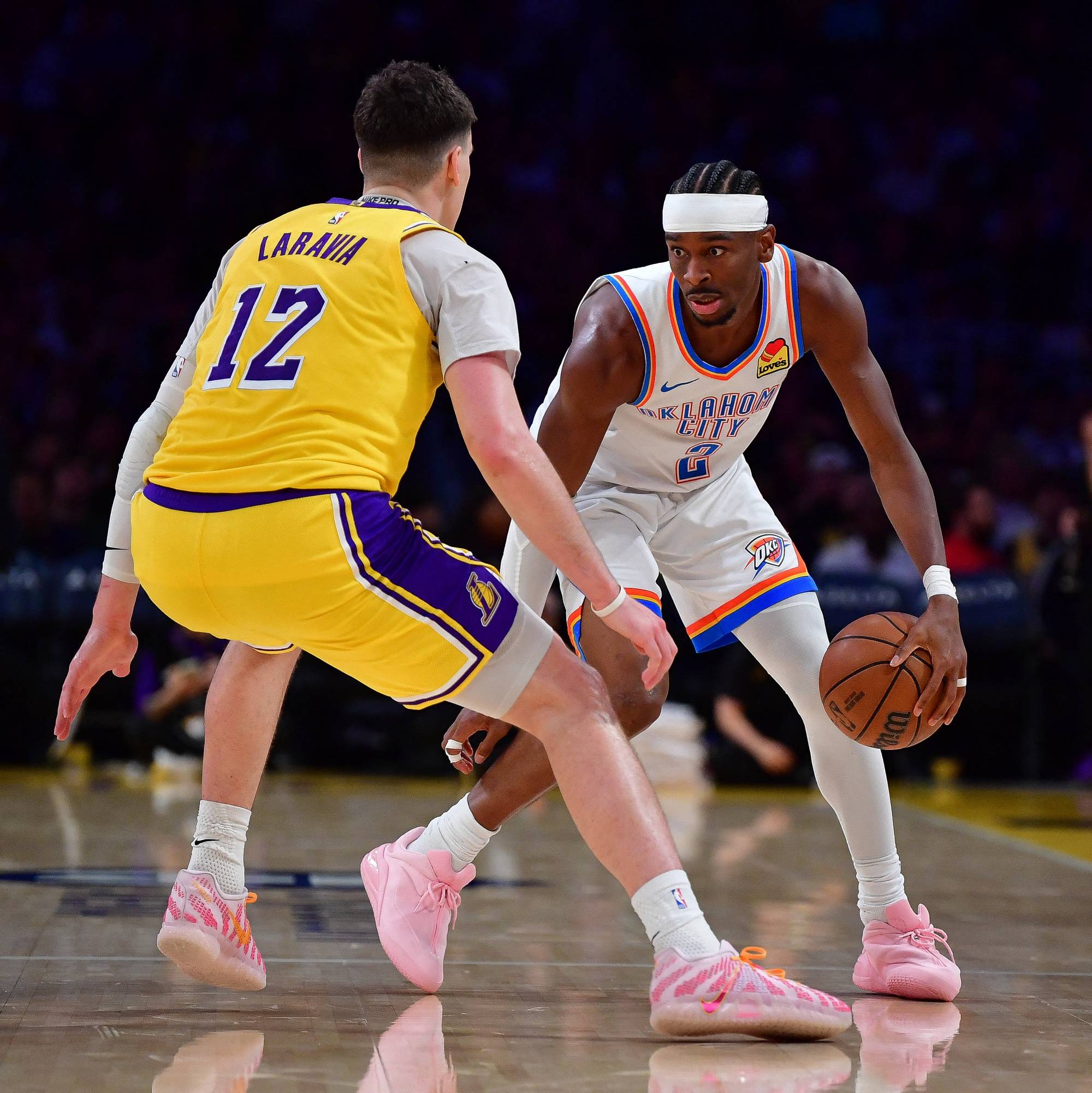 To basketballspillere er i kamp om ballen på et gulv. En spiller i gul drakt med nummer 12 og navnet Laravia på ryggen. Motspilleren, med nummer 7 på drakten, fører ballen. Publikum ser på i bakgrunnen. (Bildebeskrivelsen er laget av en KI-tjeneste)