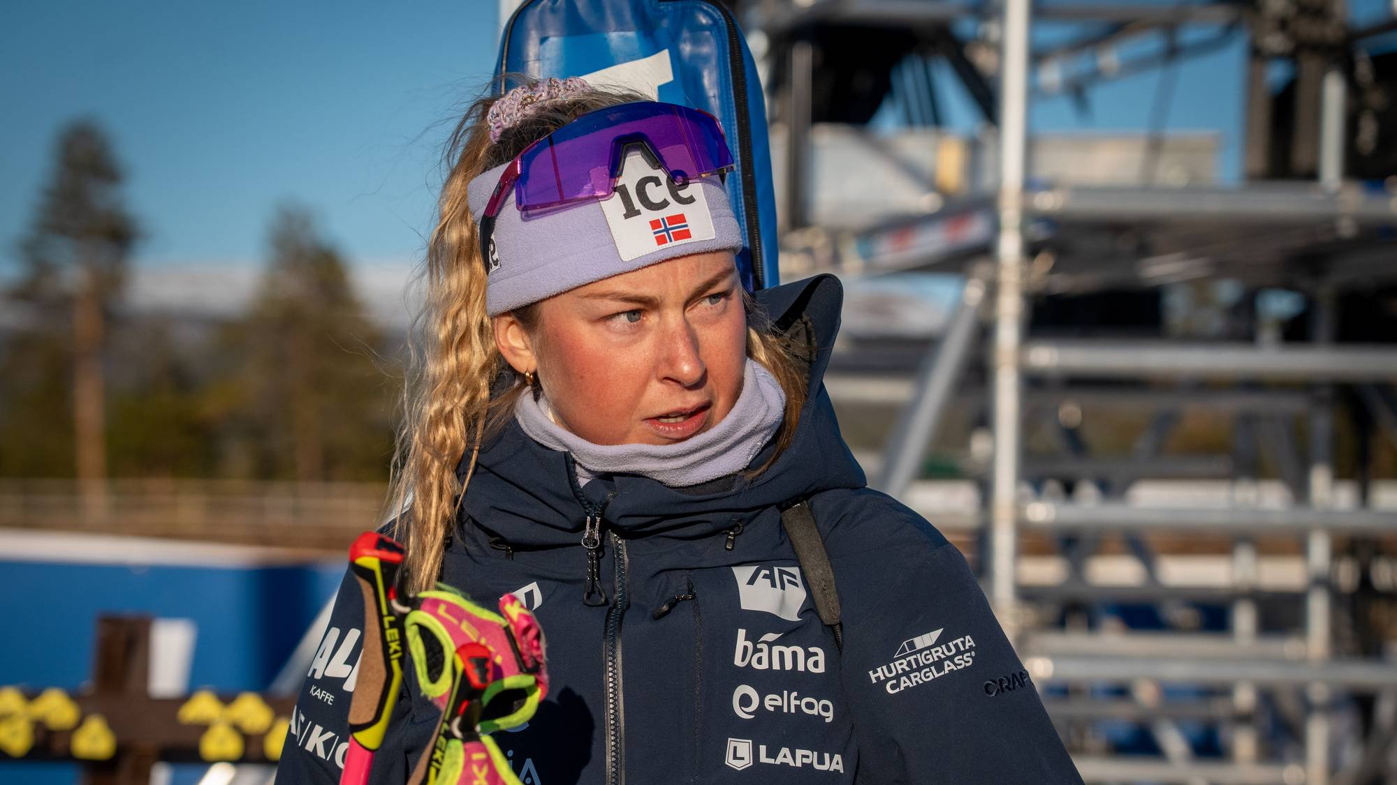 Skiskytter med pannebånd og jakke står utendørs med skistaver i hånden. (Bildebeskrivelsen er laget av en KI-tjeneste)