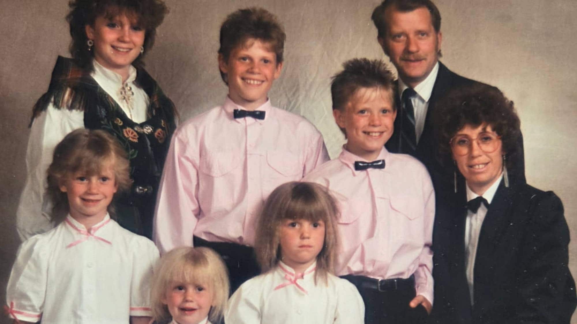 Viser en familie som står oppstilt, foran jenter i hvite kjoler, jente bak til venstre i Nordlandsbunad: To gutter i lyse skjorter med sløyfe. Foreldrene i mørke klær. 