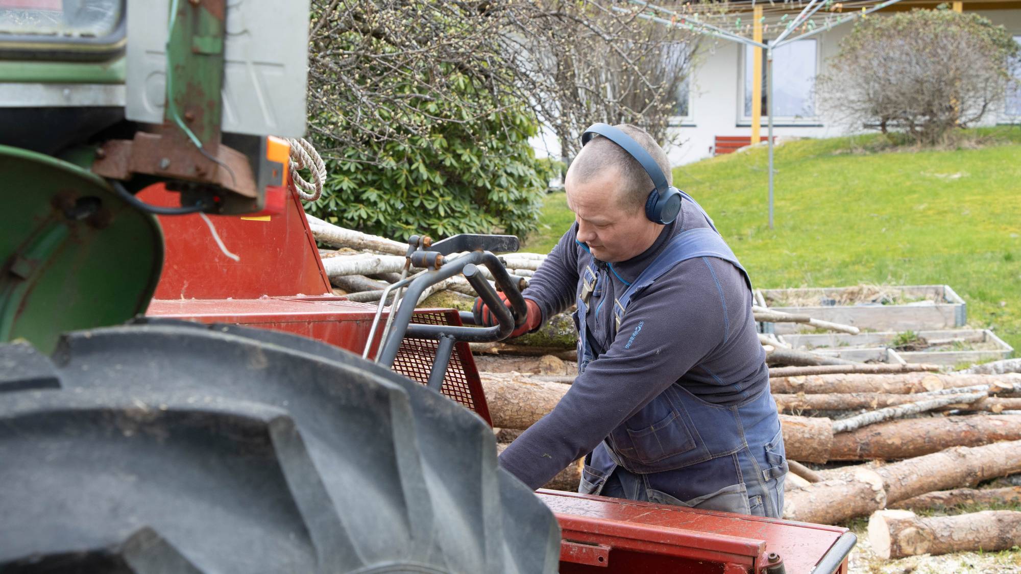 Ein mann står ved ein traktor og hoggar ved. 