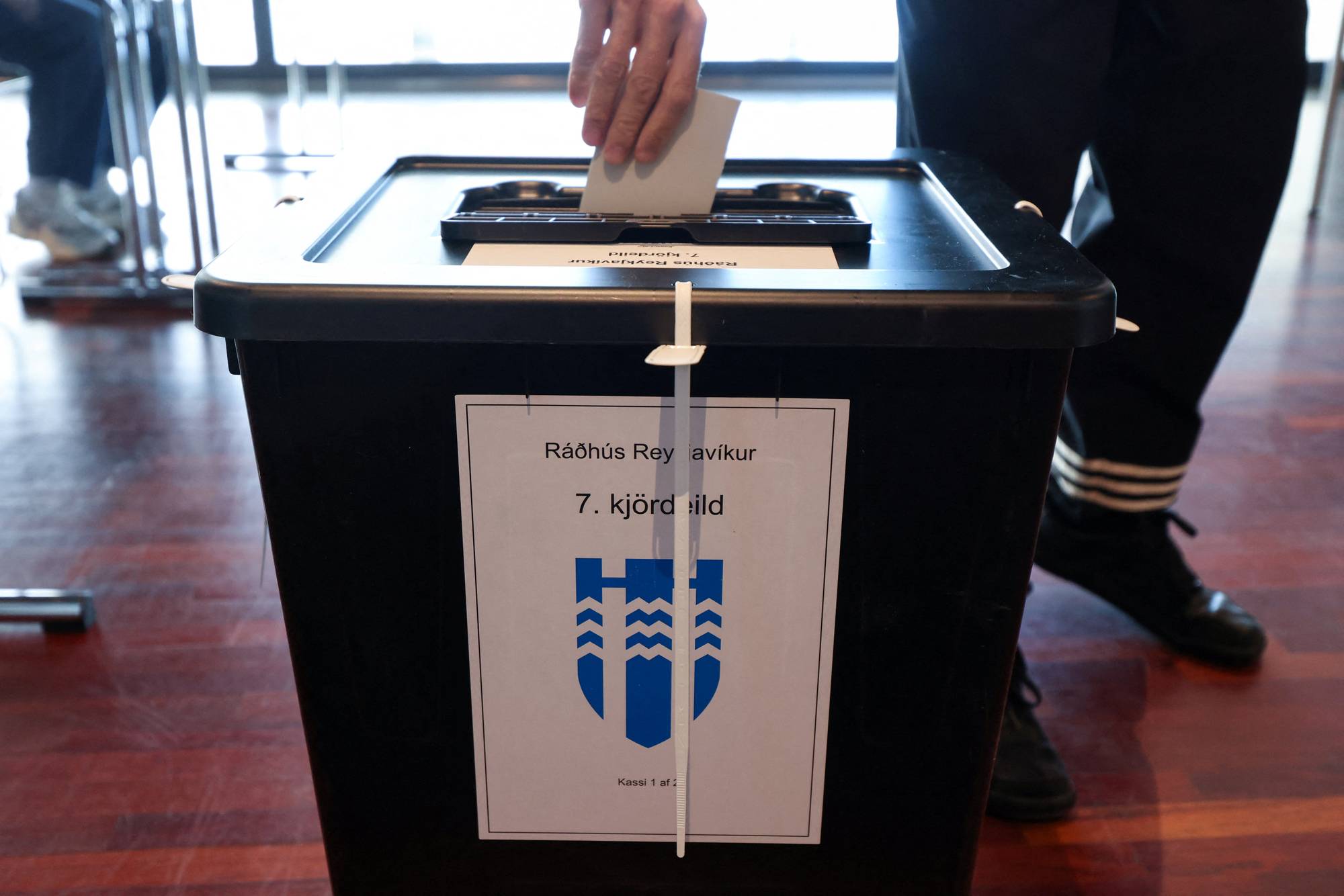 En person legger en stemmeseddel i en valgurne i Reykjavik rådhus. (Bildebeskrivelsen er laget av en KI-tjeneste)