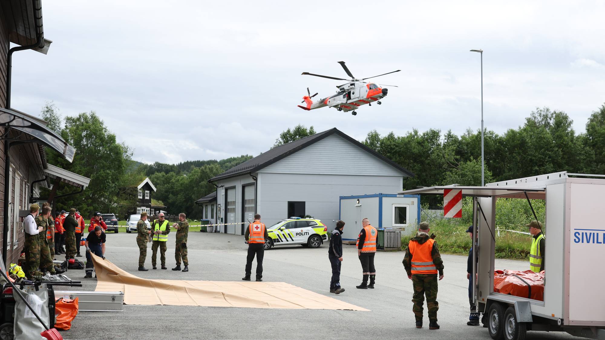 Redningshelikopter lander ved innsatssted med nødetater og mannskaper fra Sivilforsvaret. (Bildebeskrivelsen er laget av en KI-tjeneste)