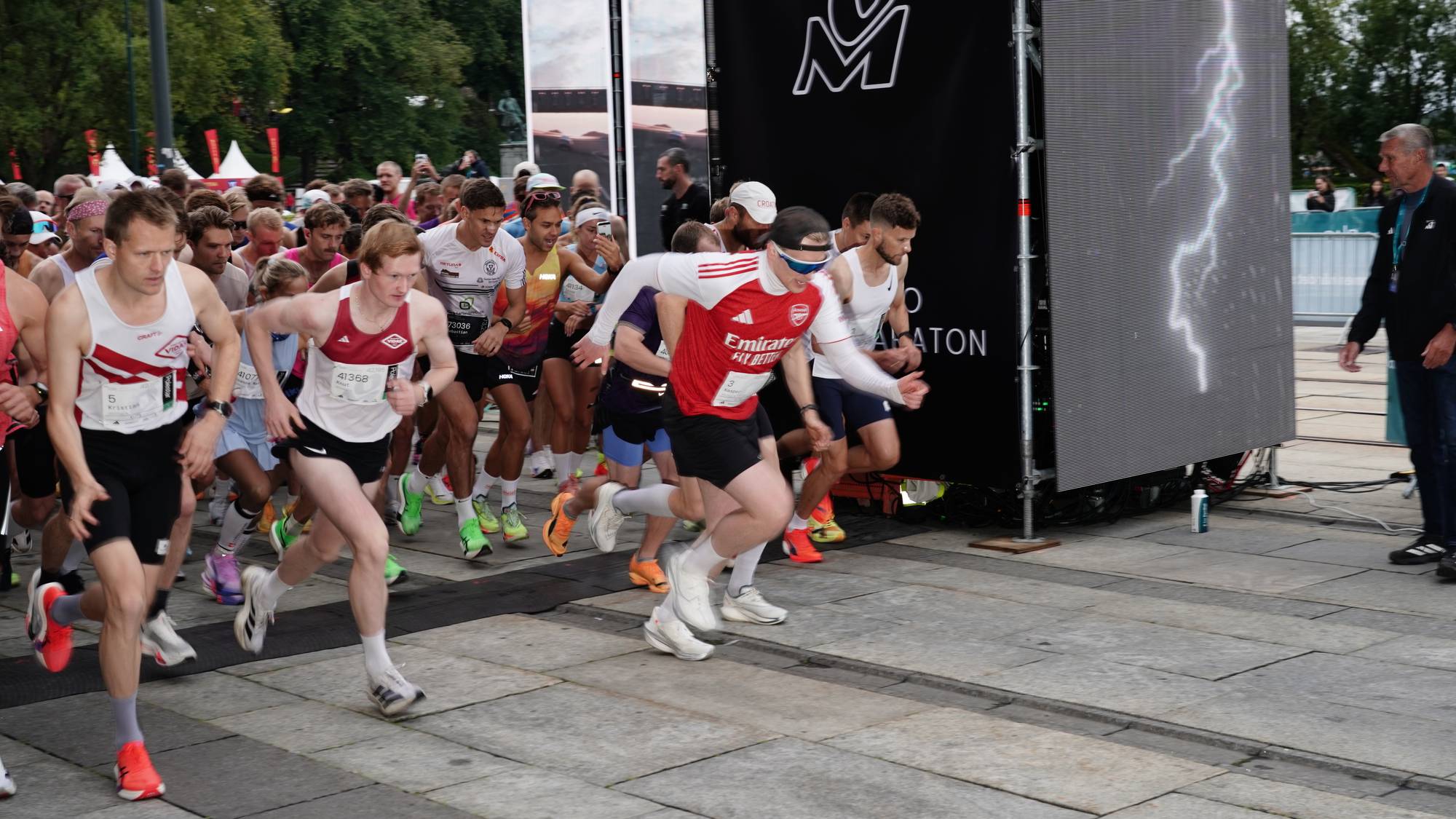 Deltakere starter løp under Oslo Maraton ved en stor skjerm. (Bildebeskrivelsen er laget av en KI-tjeneste)