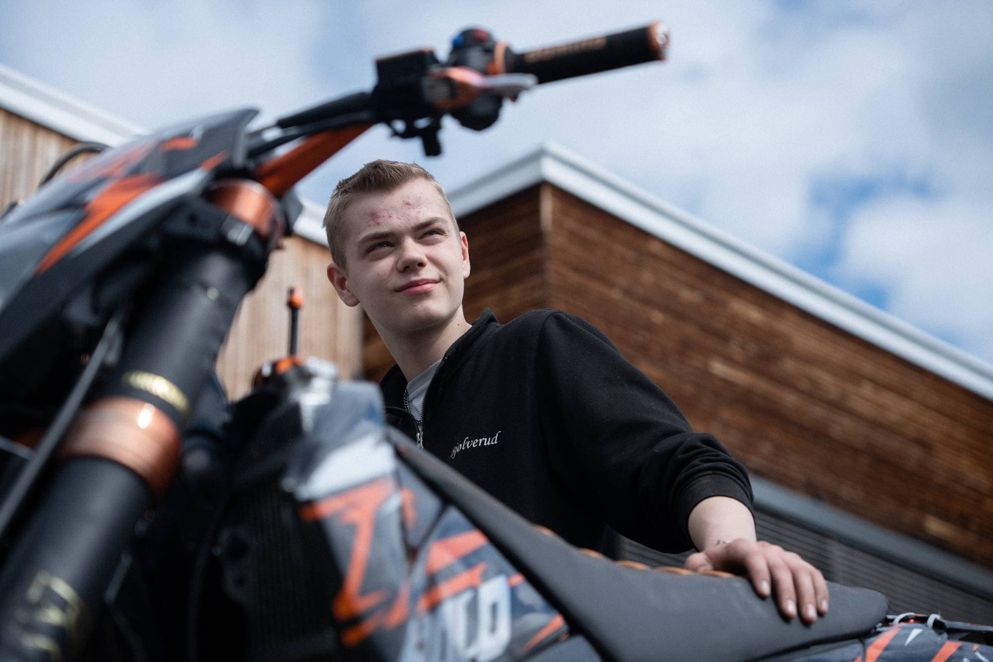 En ung mann står og lener seg på en lettmotorsykkel. 