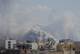NTB Røyk stiger opp fra bygninger i en by med fjell i bakgrunnen. Omgivelsene består av tettbebygde områder med varierte bygninger. En sky av grå røyk dominerer himmelen, noe som indikerer en mulig brann eller eksplosjon i området. Flere kommunikasjonsmaster er synlige i landskapet. (Bildebeskrivelsen er laget av en KI-tjeneste)