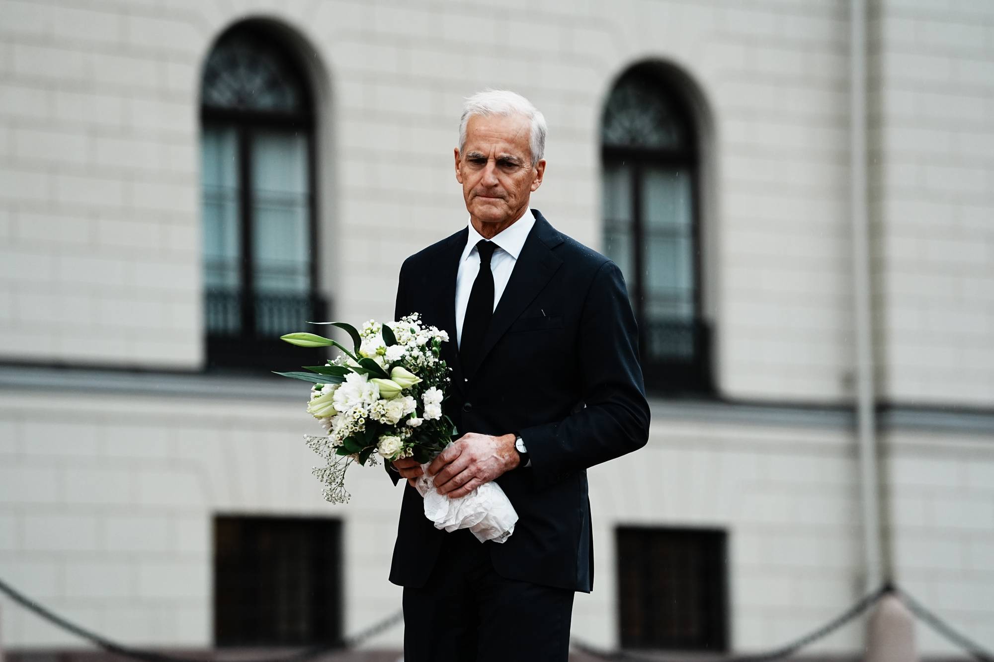 Statsminister Jonas Gahr Støre i svart dress med en blomsterbukett foran Slottet