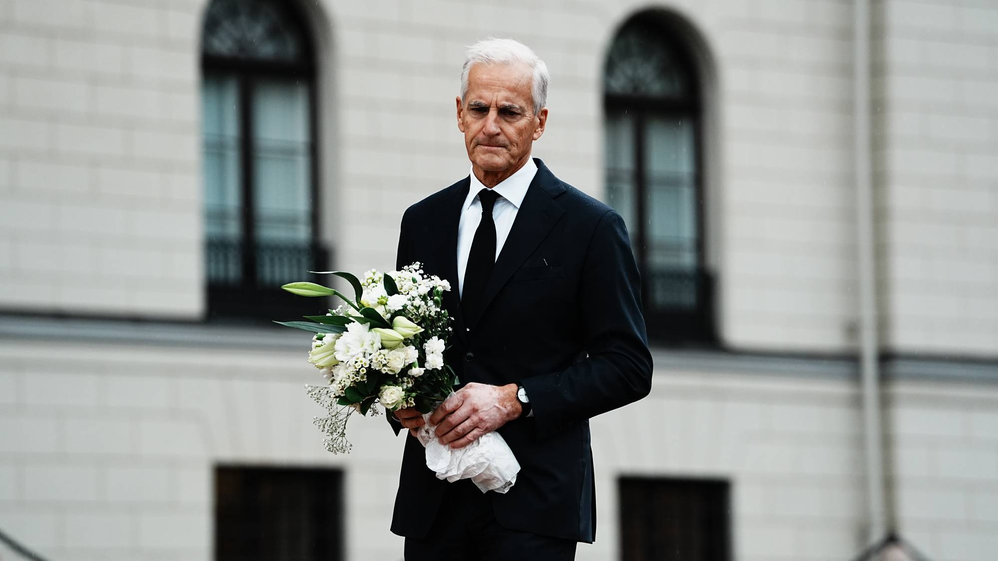 Statsminister Jonas Gahr Støre i svart dress med en blomsterbukett foran Slottet