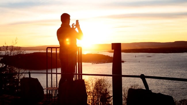 Solnedgang over sjøen. Silhuetten av en mann som tar et mobilbilde.