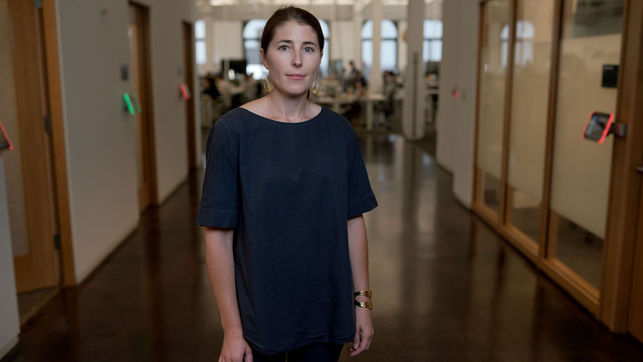 Bilde av Karina Newton, toppsjef for Instagrams retningslinjer. Hun står i en gang, og i bakgrunnen det et kontor med ansatte som jobber. Ansiktsuttrykket er nøytralt.