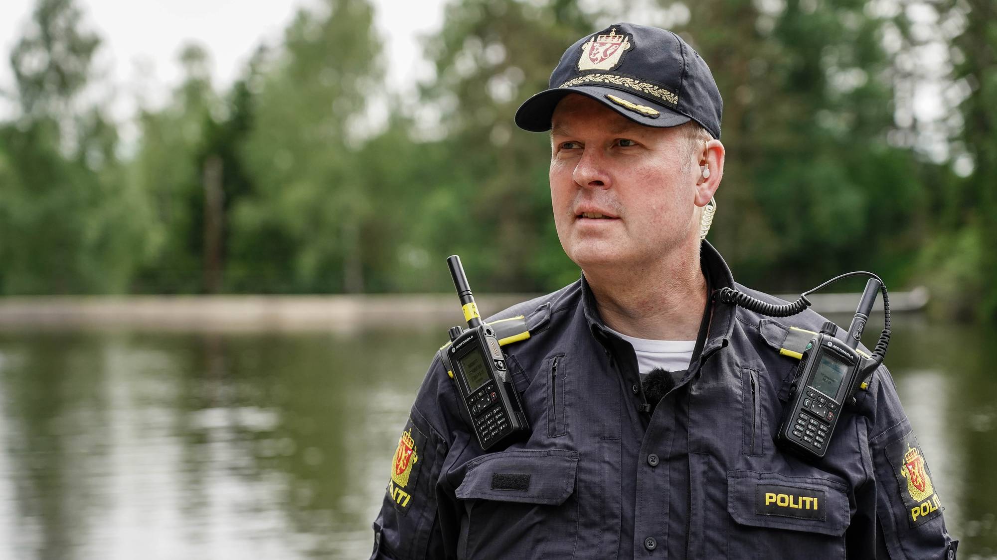En norsk politimann i uniform står utendørs ved et vann. (Bildebeskrivelsen er laget av en KI-tjeneste)