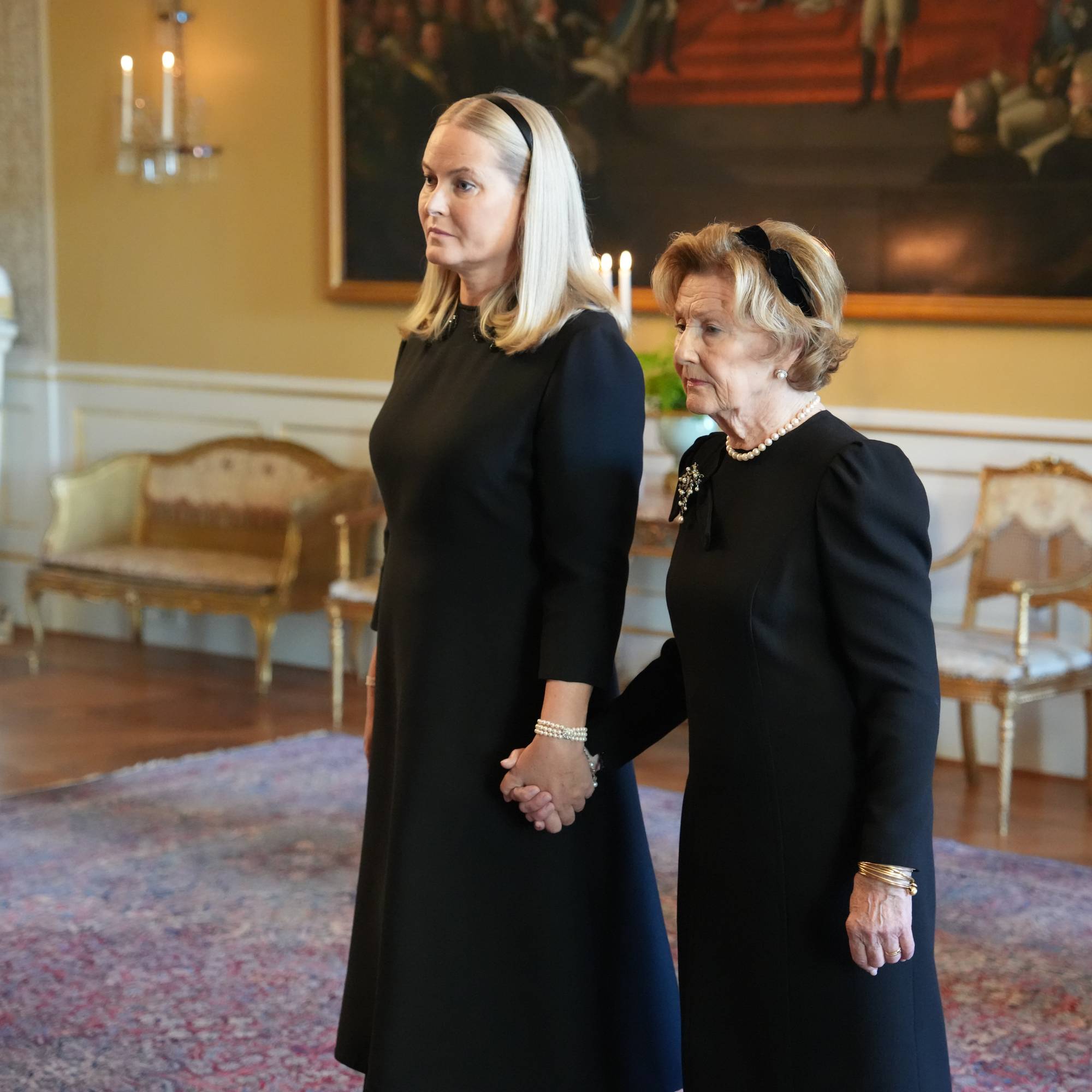 Kronprinsesse Mette-Marit og dronning Sonja holder hverandre i hendene i en stue på Slottet. (Bildebeskrivelsen er laget av en KI-tjeneste)