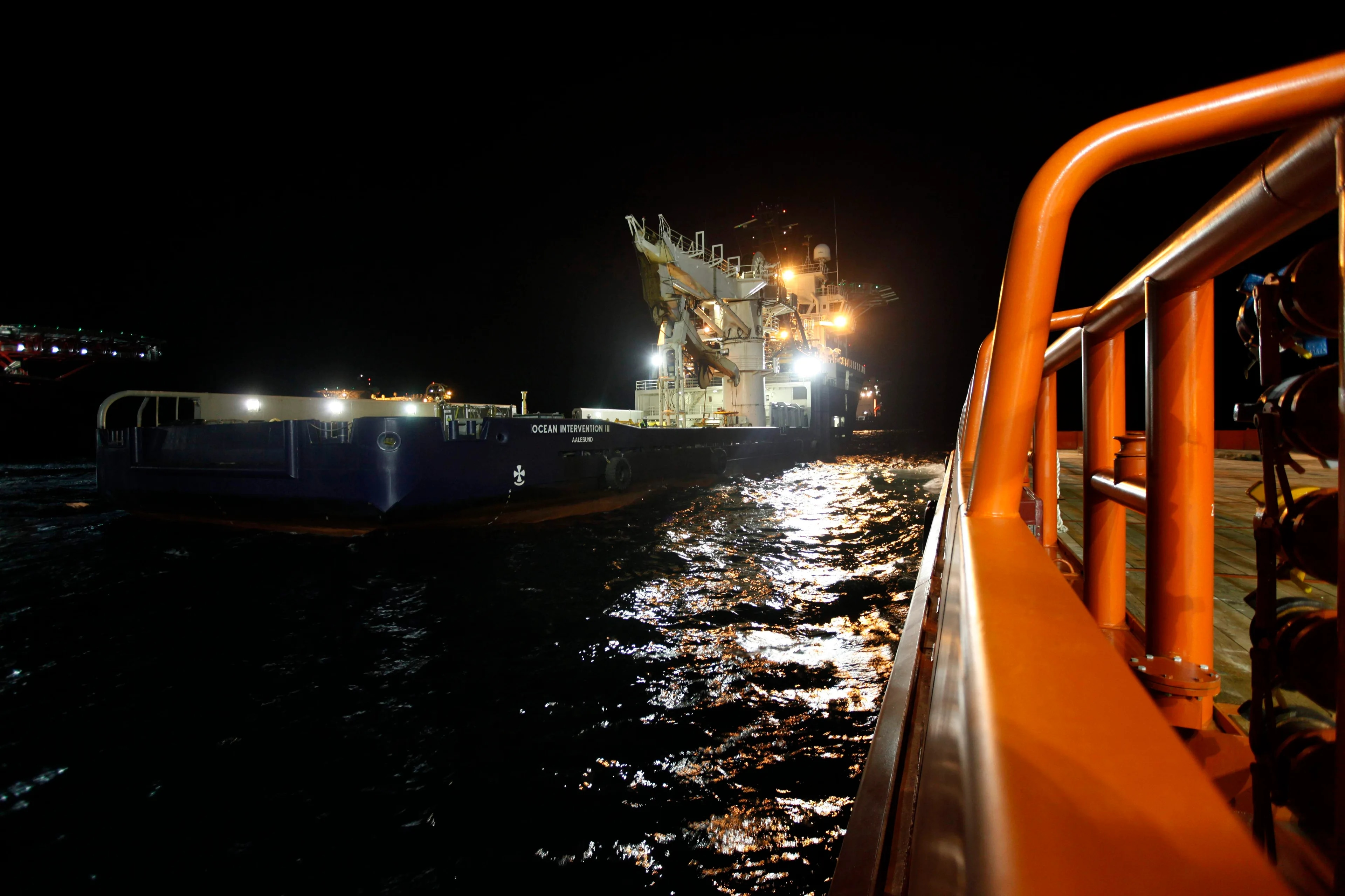 Det er mørkt og lyset fra Ocean Intervention III reflekteres på det mørke vannet. I forgrunnen ser en deler av et annet skip som er orange. Det er kveld i mai 2010 og det norske skipet jobber med å stenge oljebrønnen.