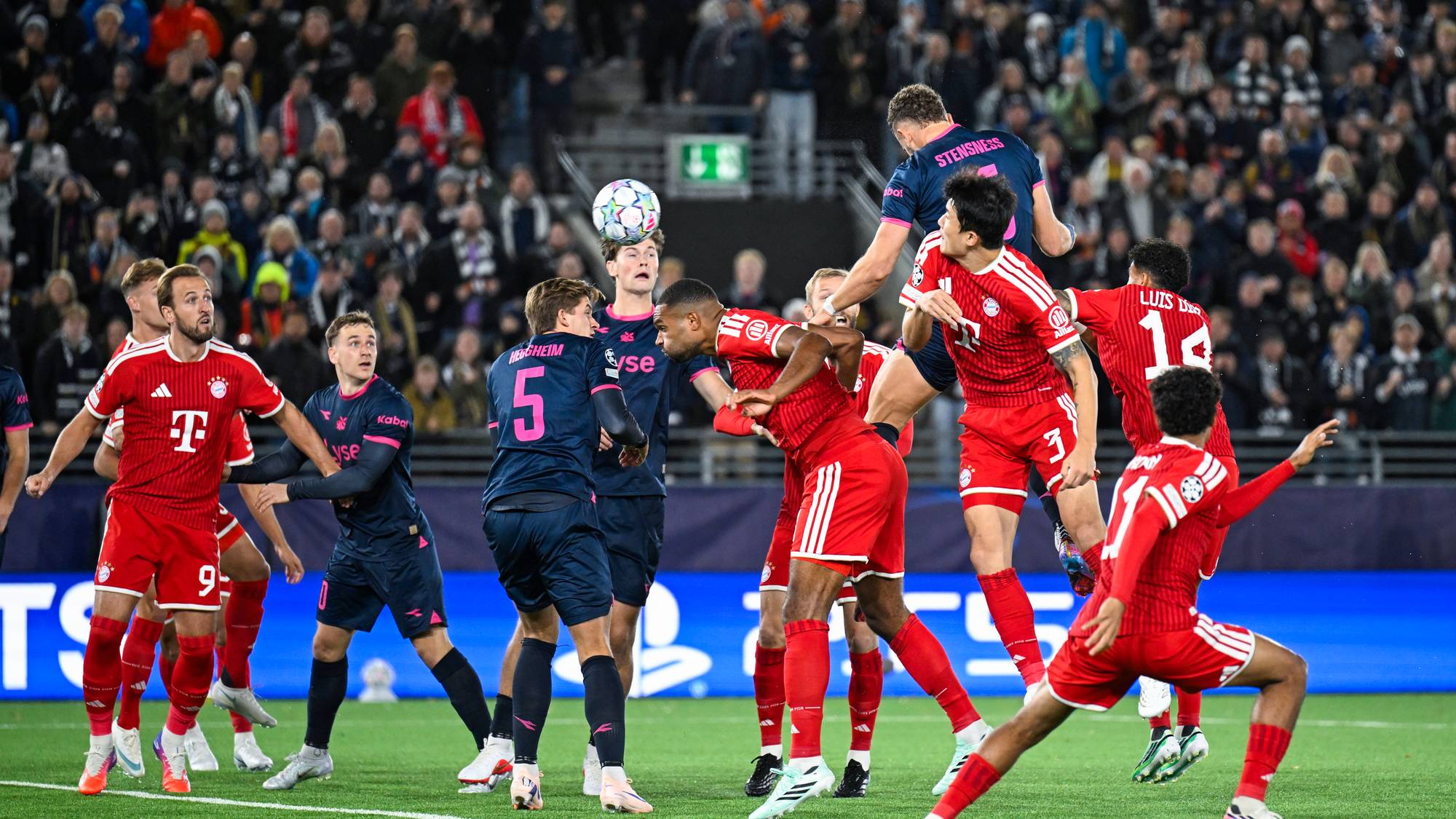Fotballspillere fra Viking og Bayern München kjemper om ballen i luften foran et fullsatt stadion. (Bildebeskrivelsen er laget av en KI-tjeneste)